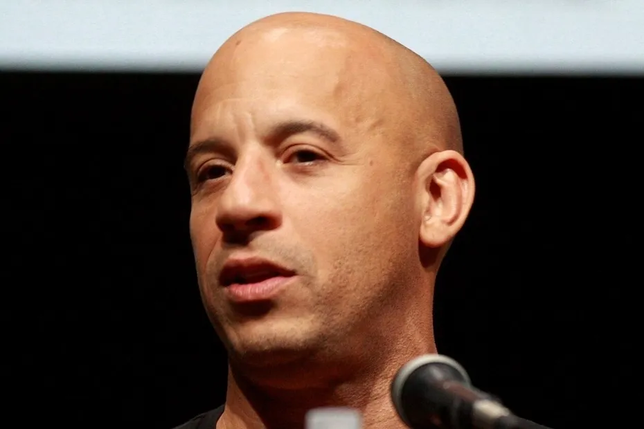 Close-up of bald Vin Diesel speaking into a microphone, known for the catchphrase "I'll be back".