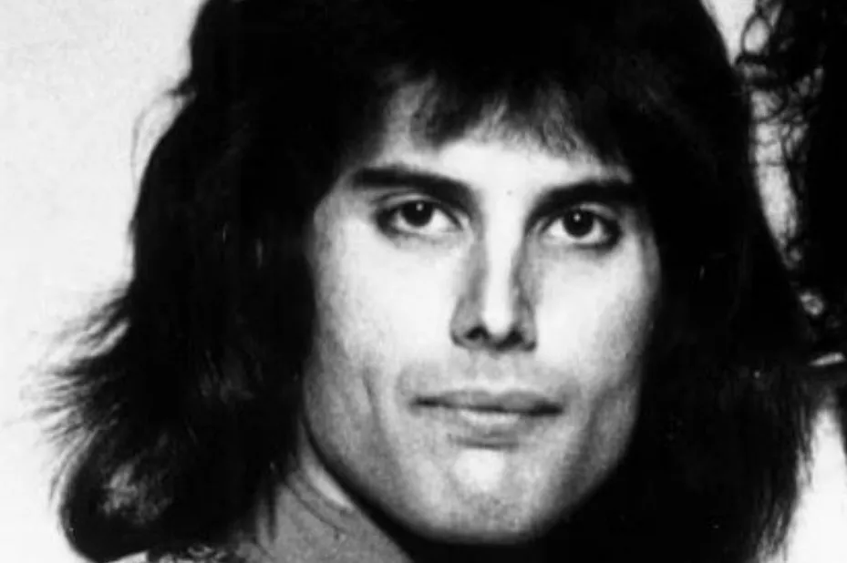 Black and white close-up photo of young Freddie Mercury with long, dark hair and intense eyes, looking forward.