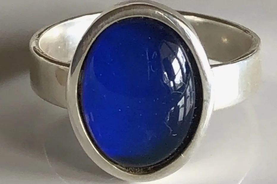 A close-up of a Mood Ring, an 80s fashion accessory, showing its blue, oval-shaped stone set in a silver band.