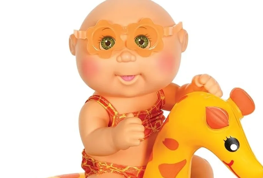 A bald Cabbage Patch Kids doll in orange sunglasses and a red swimsuit, riding a yellow giraffe toy.