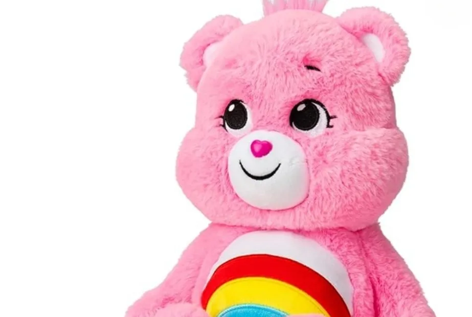 A close-up of a pink Care Bear stuffed toy with a rainbow on its belly, smiling sweetly.
