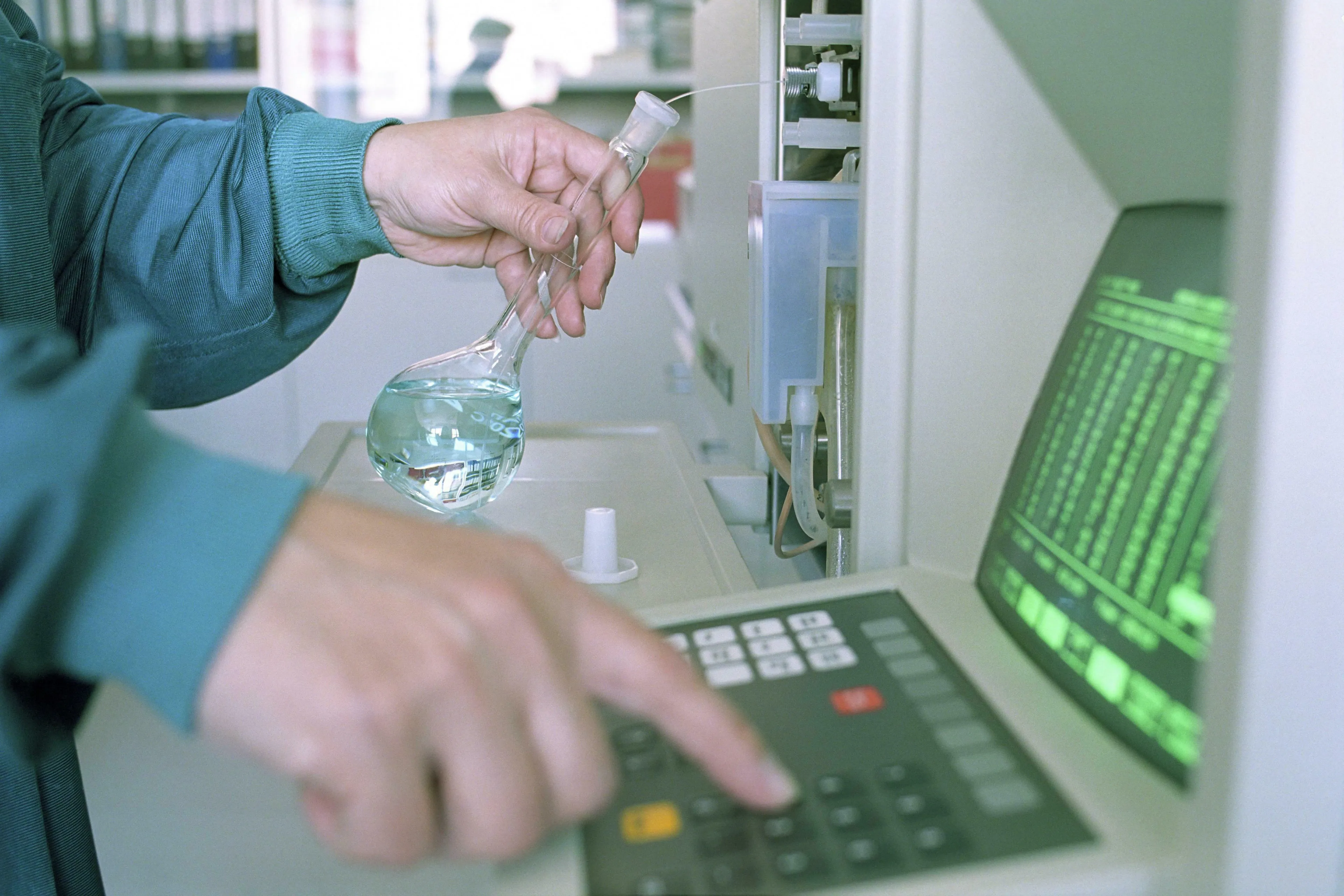 Scientist conducting a science general knowledge experiment, holding a flask and using a machine to measure acidity/alkalinity.