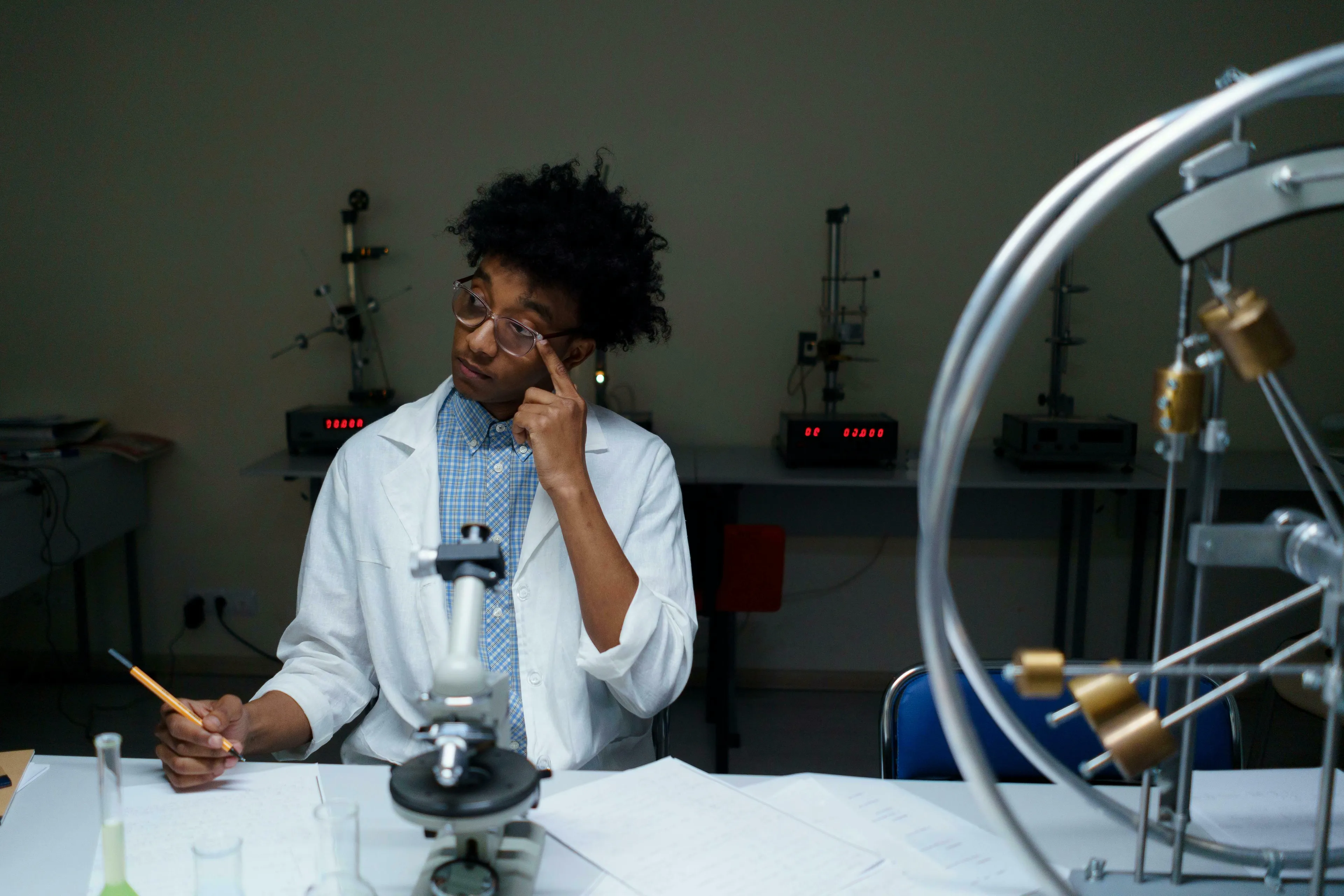 A male student in a lab coat and glasses, writing at a desk with a microscope. Science general knowledge quiz, what is osmosis?