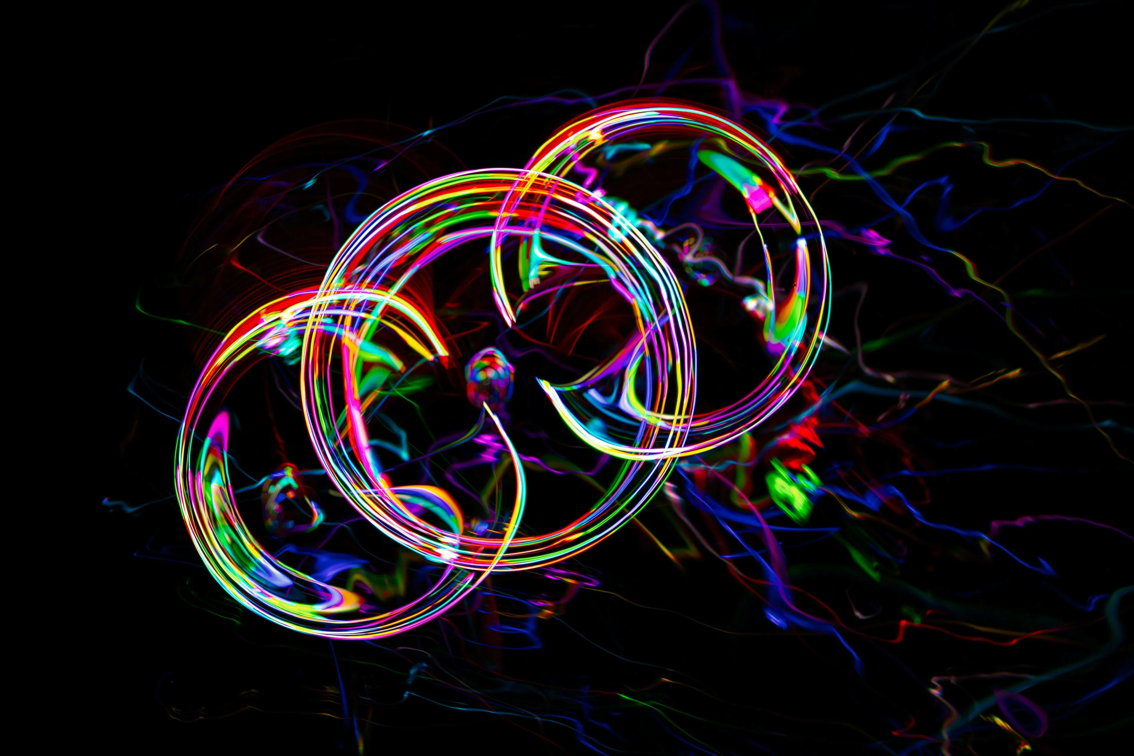 Vibrant light trails form intertwined rings and swirling lines against a dark background, representing quantum theory phenomena. Science General Knowledge Quiz.