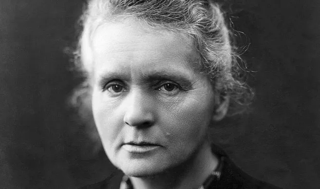 A black and white close-up of Marie Curie, scientist, looking directly at the viewer with a serious expression.