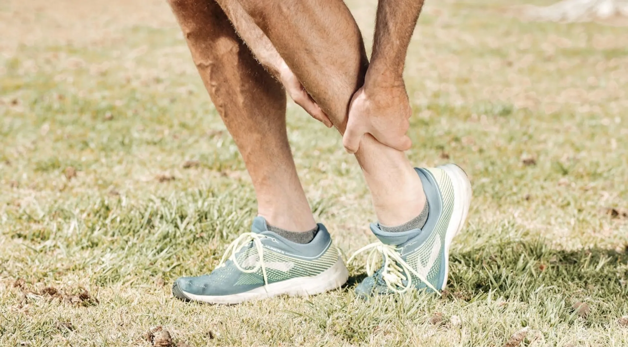 A person clutching their twisted ankle in pain on a grassy field, highlighting the need for first aid and survival skills.