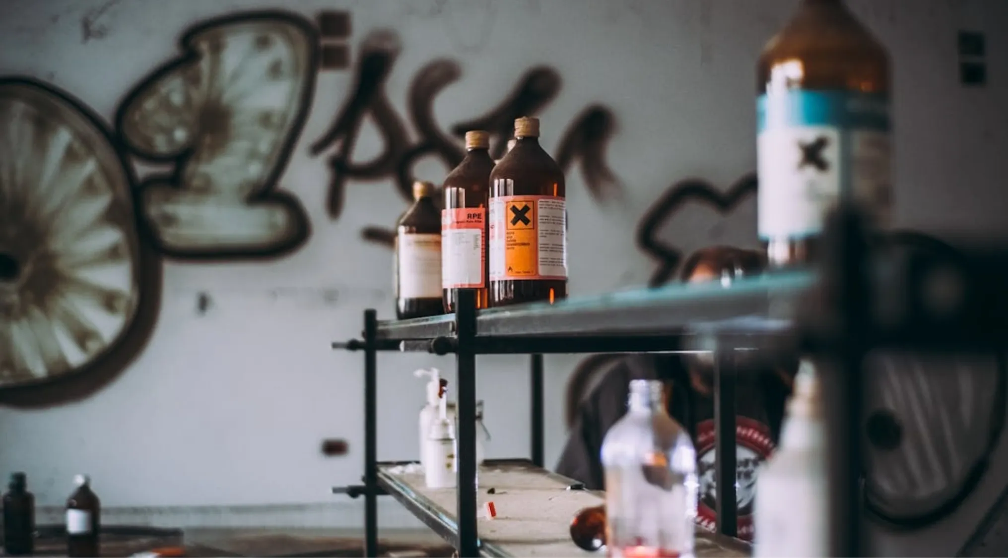 Bottles with warning labels on shelves against a graffitied wall, related to first aid for toxic substance exposure.