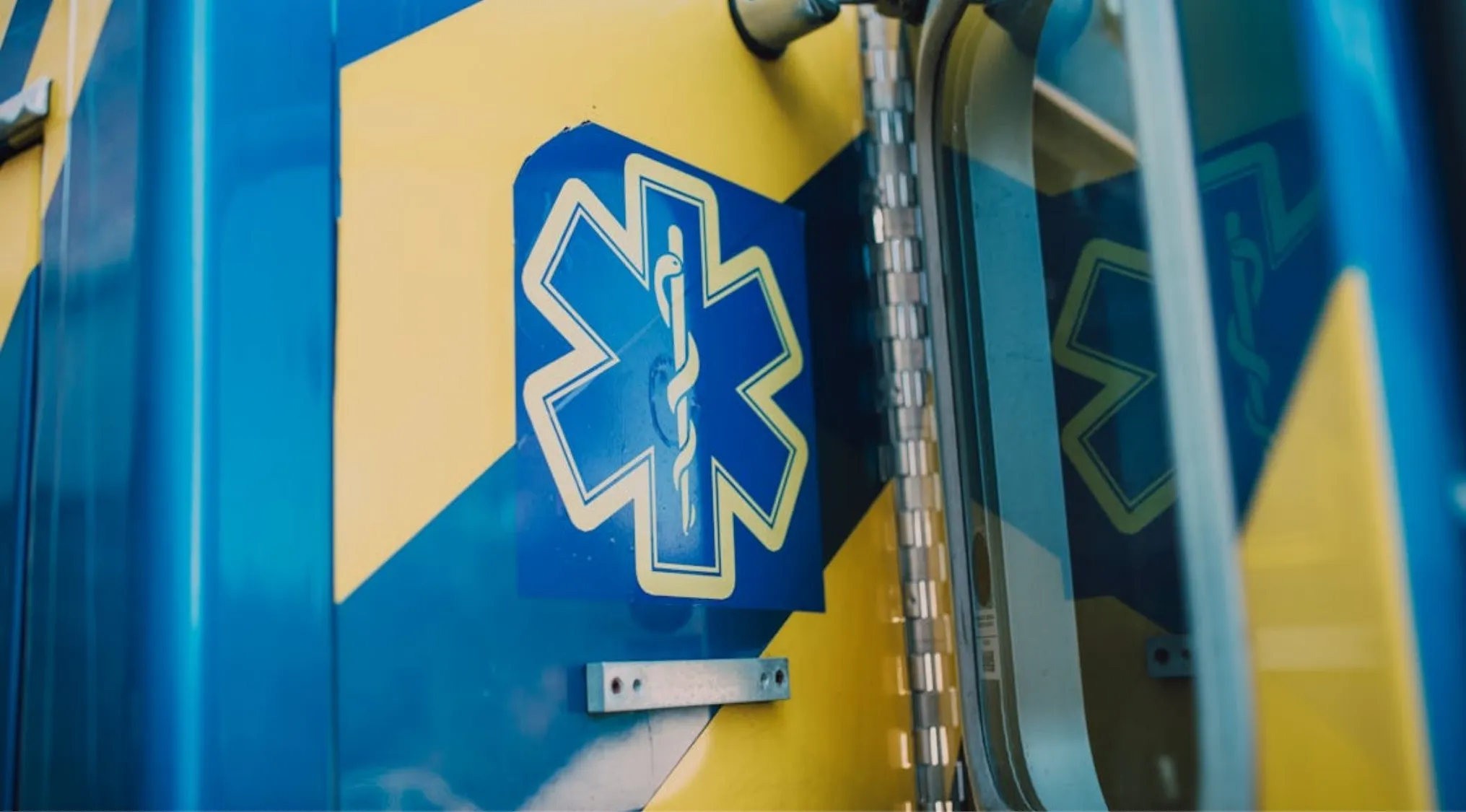 Close-up of an ambulance side with the blue Star of Life emblem on a blue and yellow background. Focus on first aid and survival.