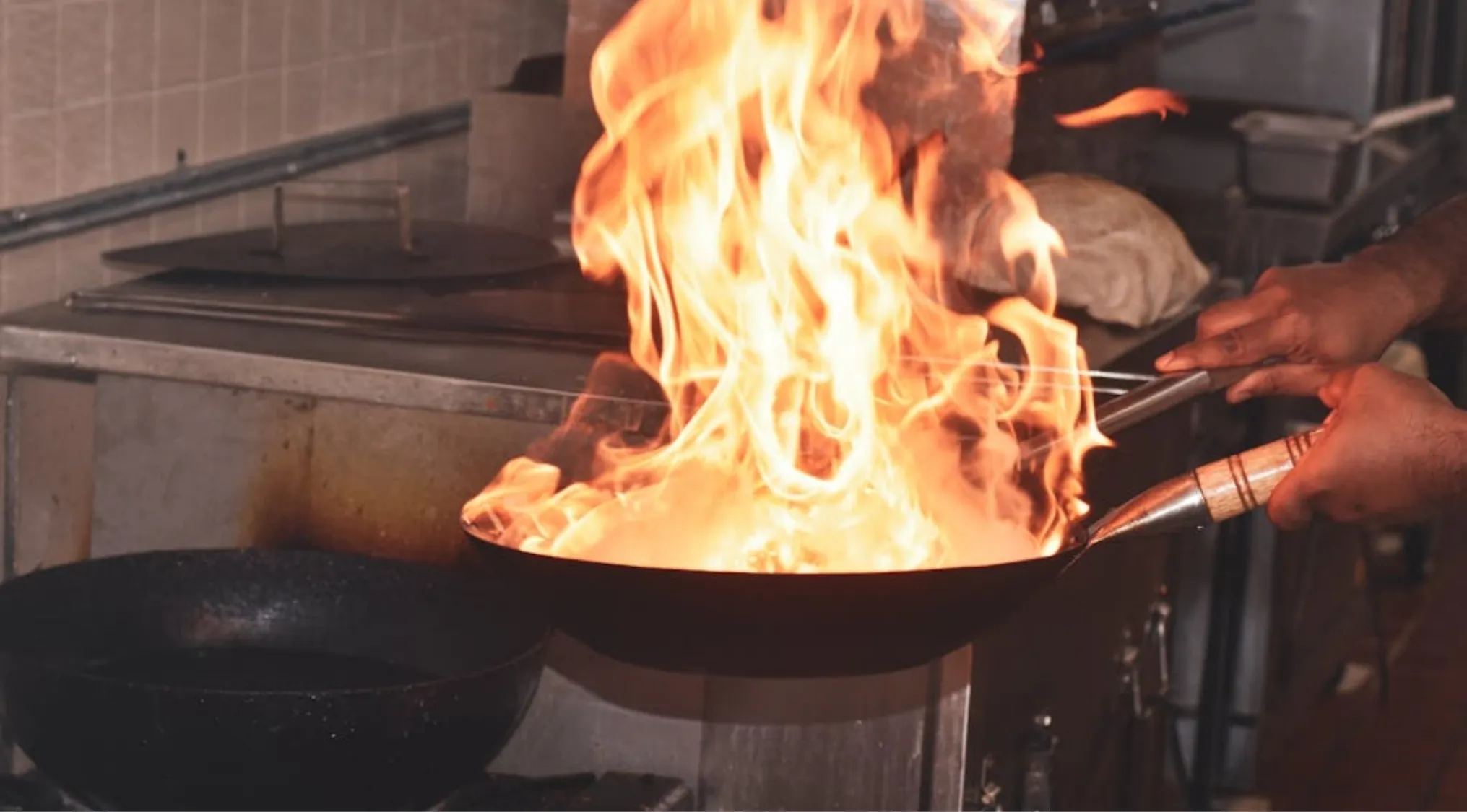 Hands cooking with high flames in a wok, illustrating a kitchen emergency for first aid survival.