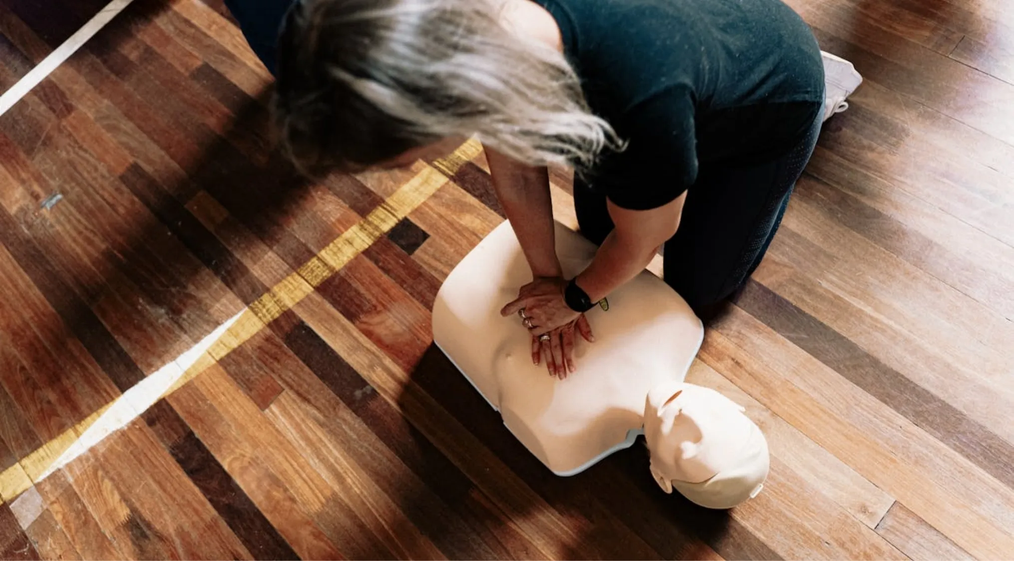 Woman performing chest compressions on a First Aid CPR mannequin, practicing survival skills for emergencies.