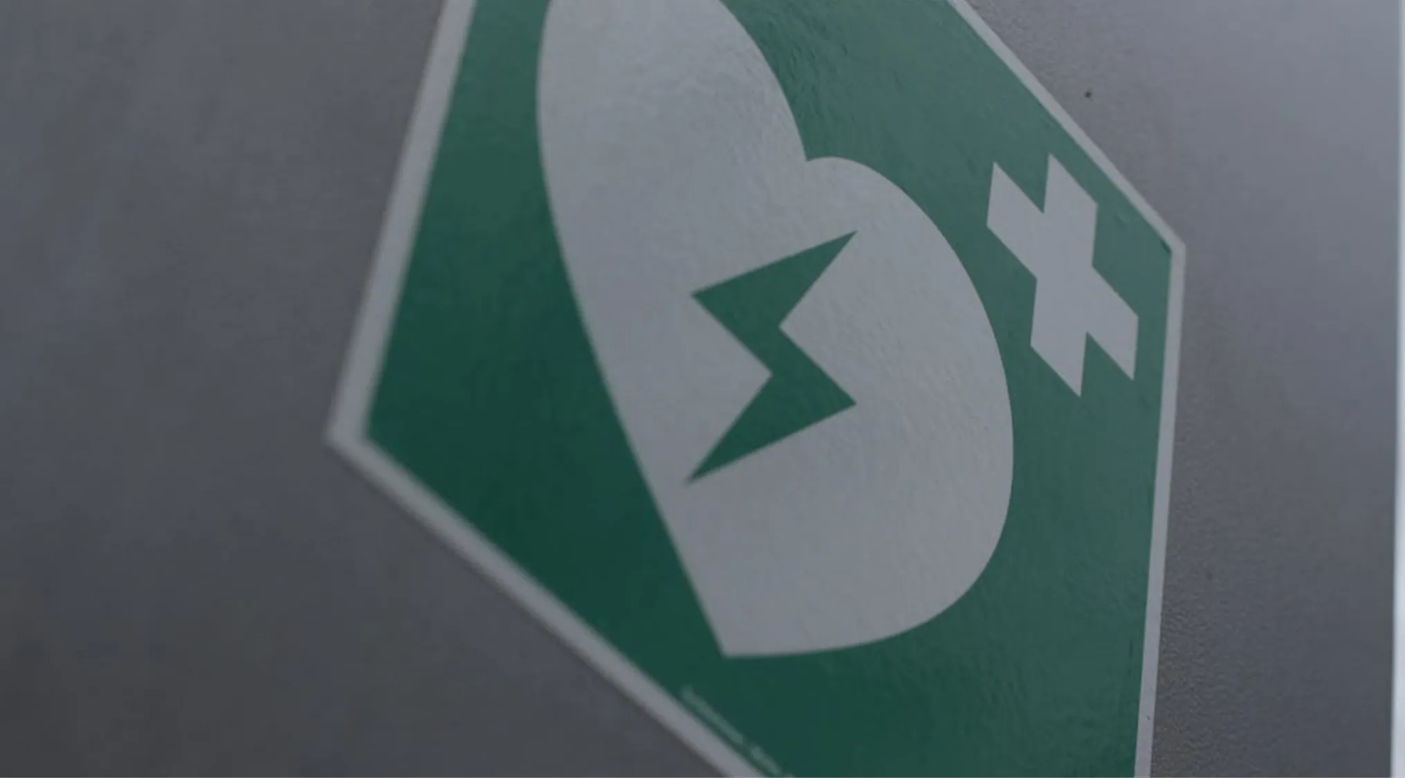 A green AED and first aid sign on a gray wall. Important for Survival 101: CPR for an infant.