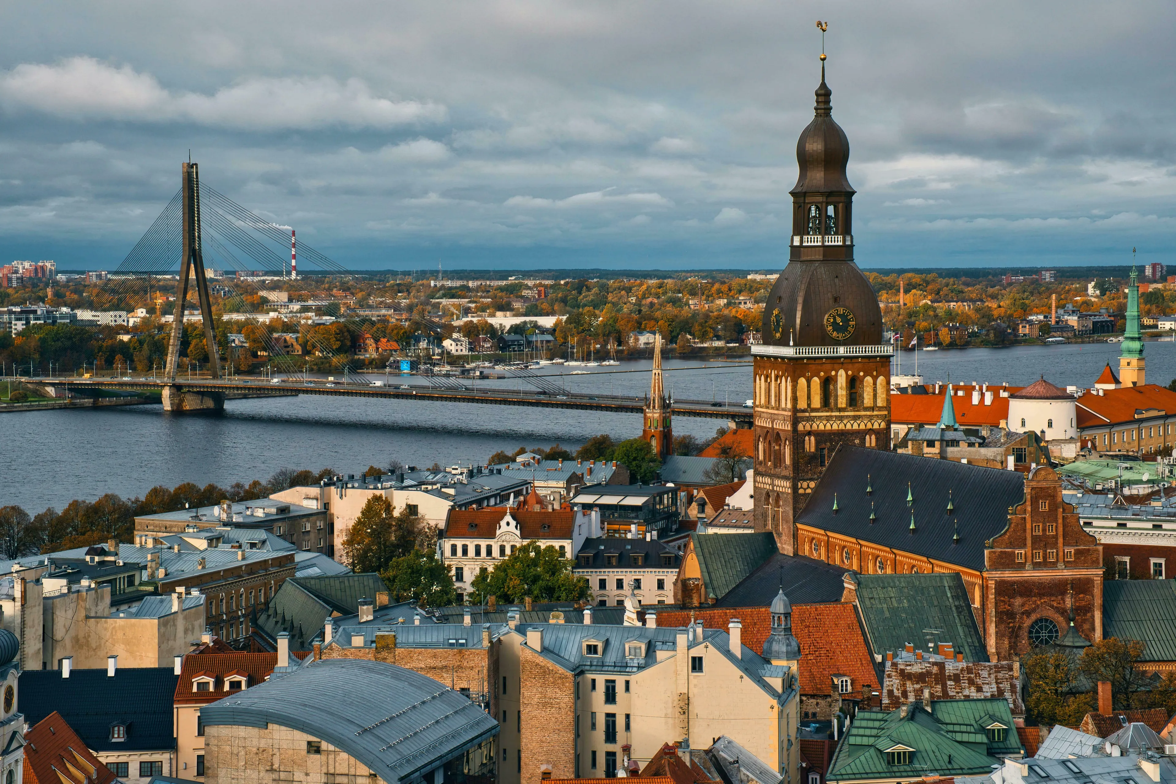 An aerial view of Riga, Latvia, featuring the Daugava River, a cable-stayed bridge, and the Old Town with its towering cathedral, contributing to British vocabulary.