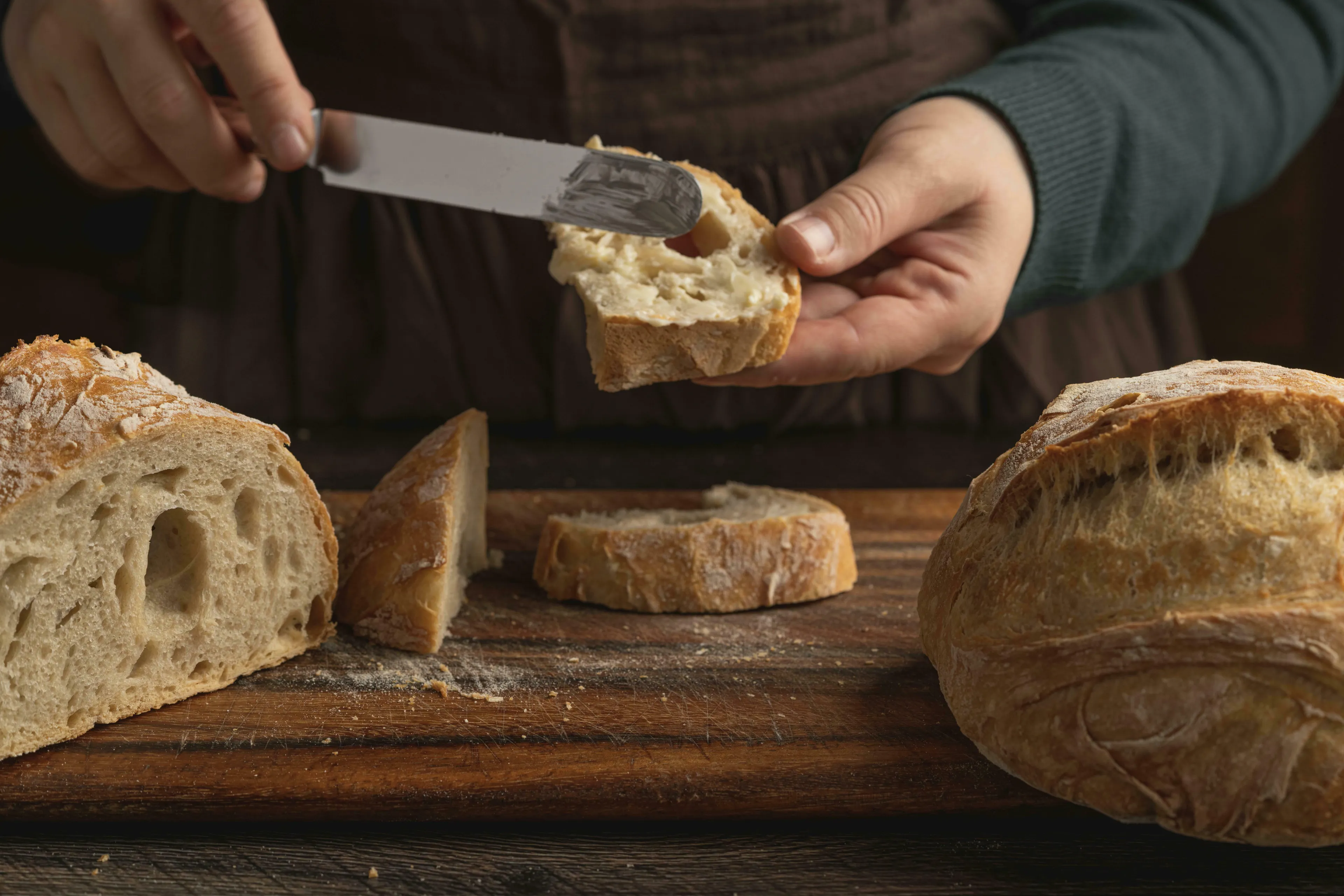 Hands buttering a slice of bread on a wooden board, with more bread. Great British vocabulary quiz about butter up.