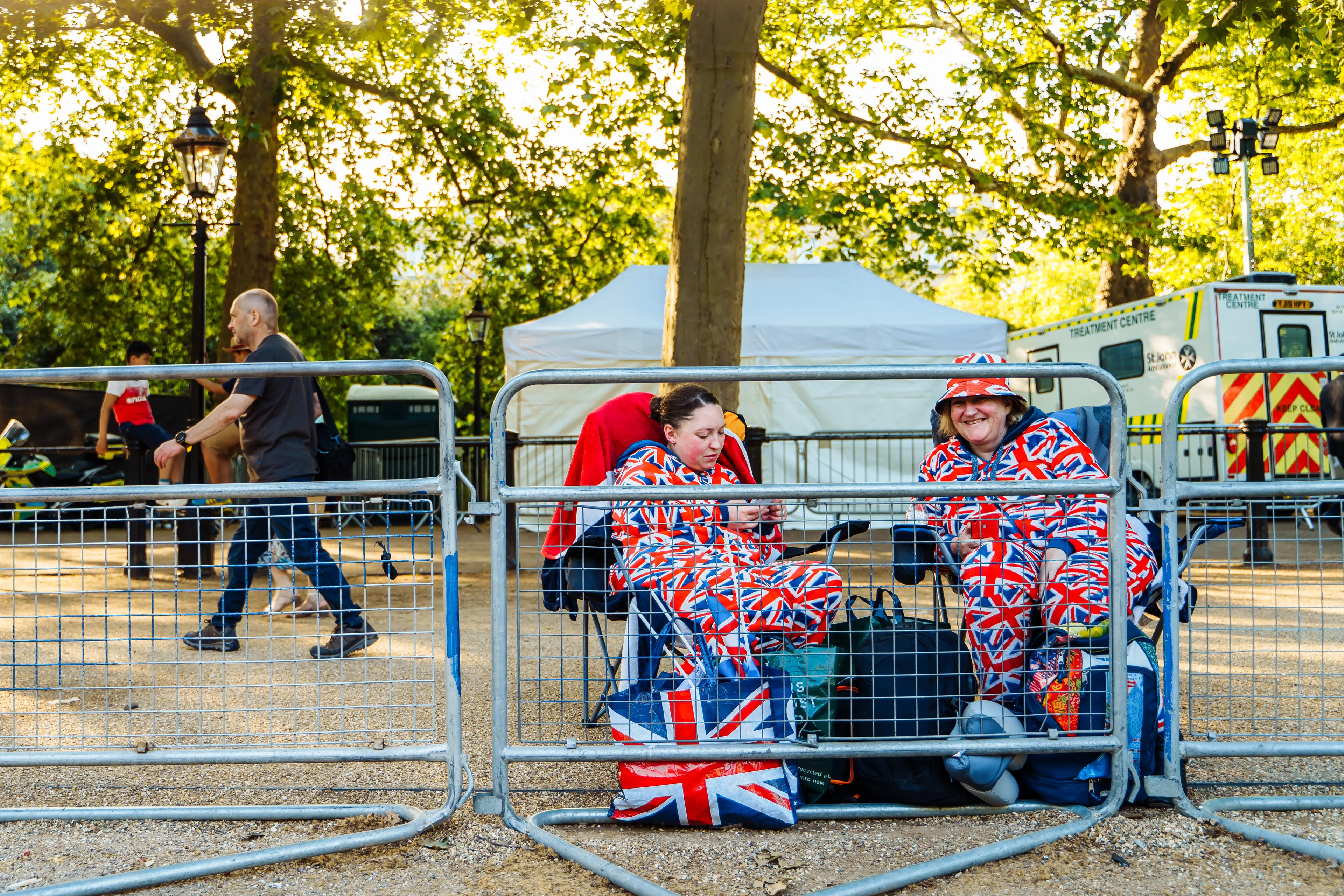 Two women in Union Jack attire sit behind metal barriers, perhaps having a bit of a moan while waiting. British vocabulary.