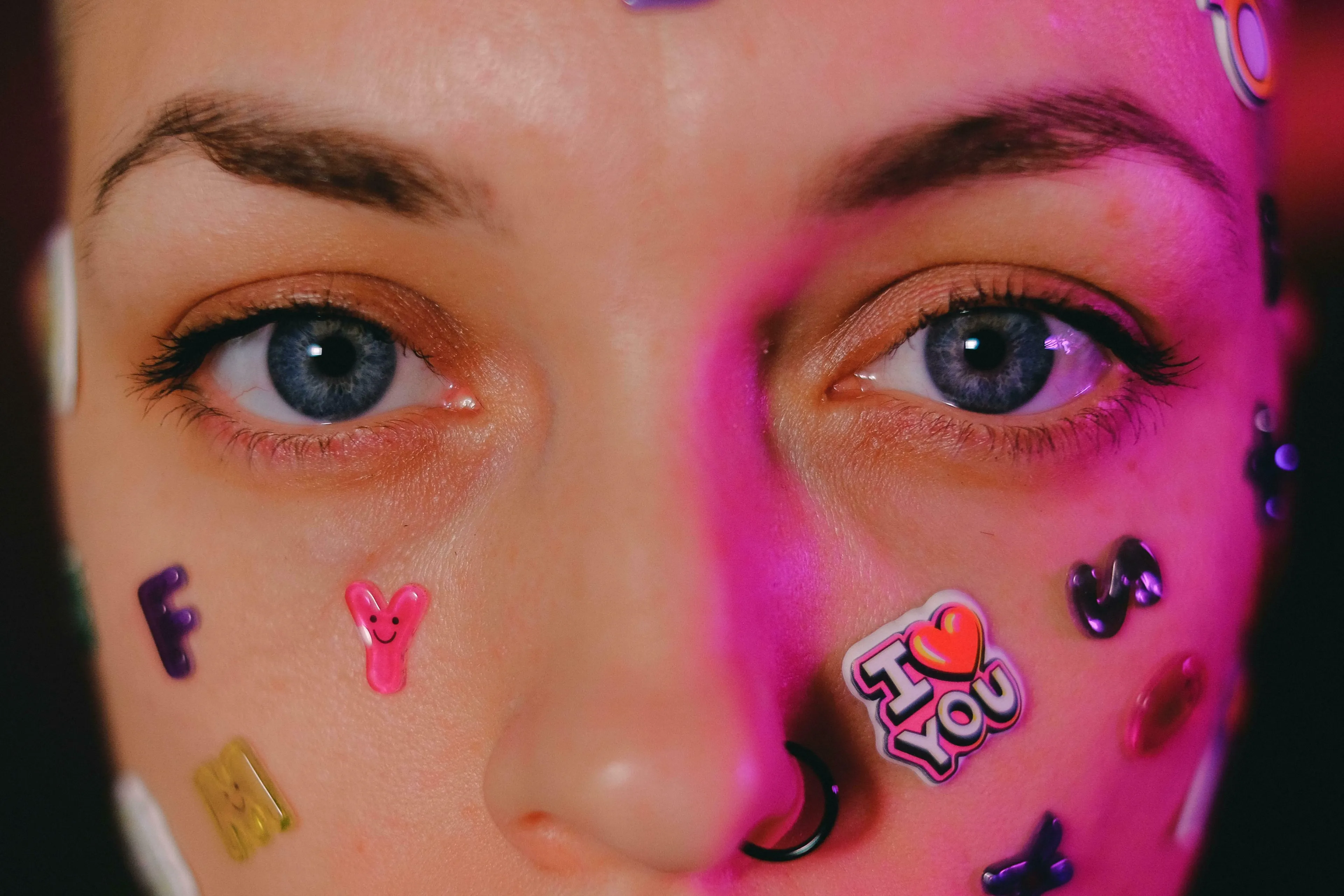 Close-up of a person's face with stickers, dark blue eyes, and pink lighting. British Vocabulary Quiz: on the blink.