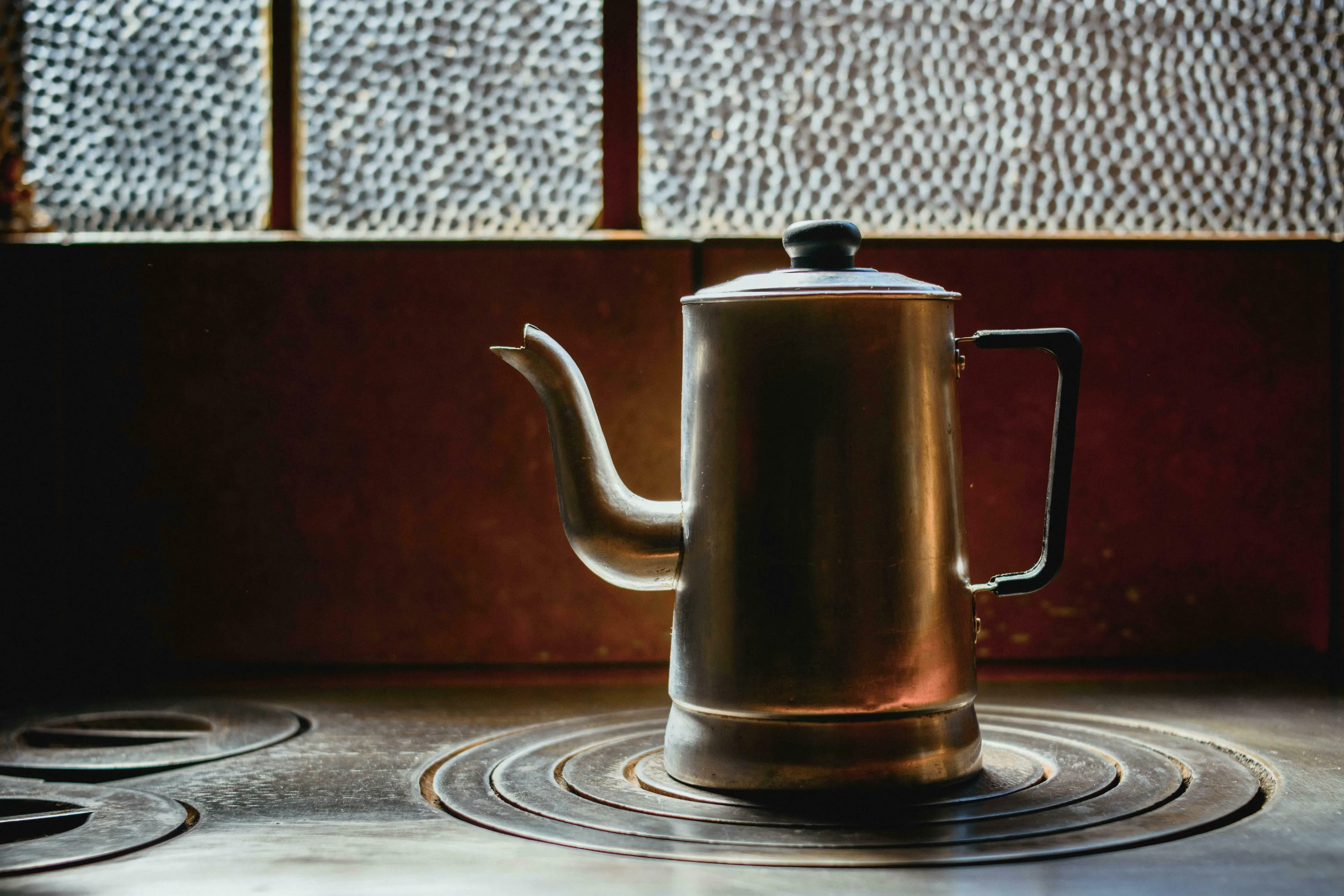 An old metal kettle on a stove, against a textured glass window, for a British Vocabulary Quiz about making tea.