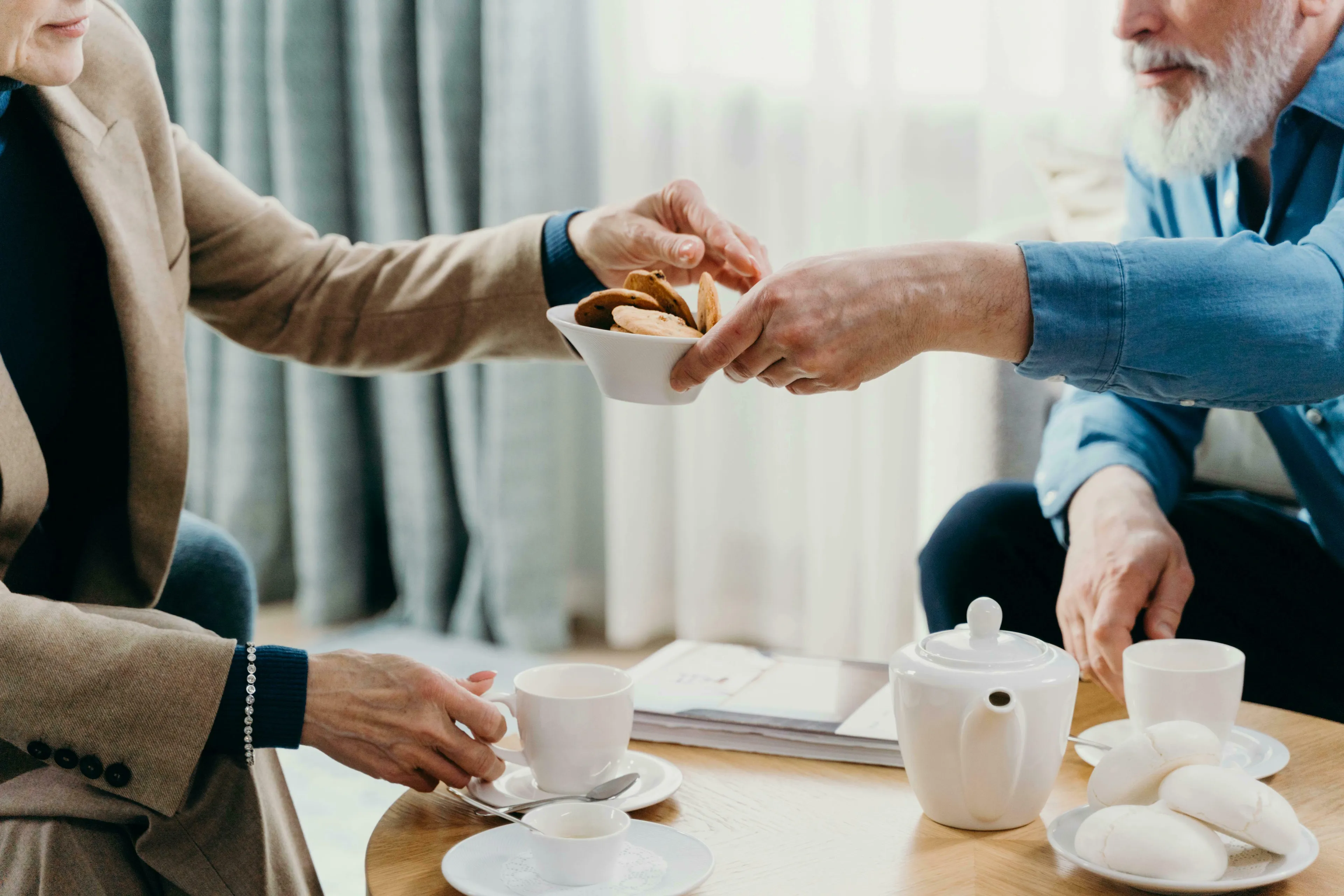 Two people sharing biscuits and tea, illustrating British vocabulary. One hand offers a bowl of cookies, while another holds a teacup.