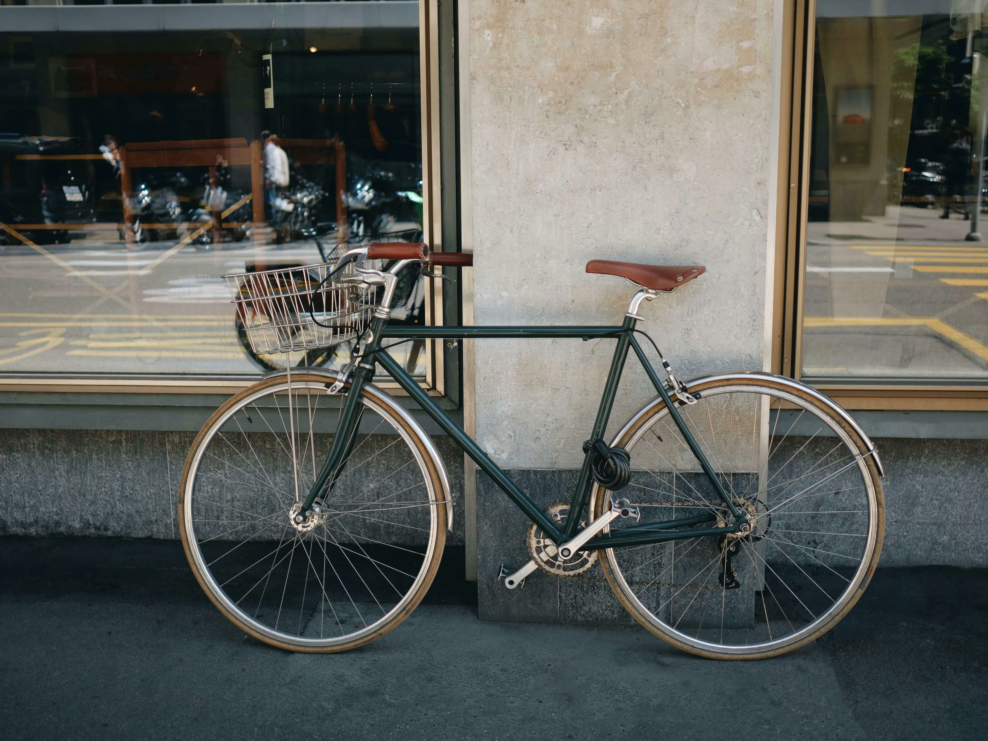 A dark green bicycle with a front basket and brown seat, leaning against a building. British vocabulary quiz.