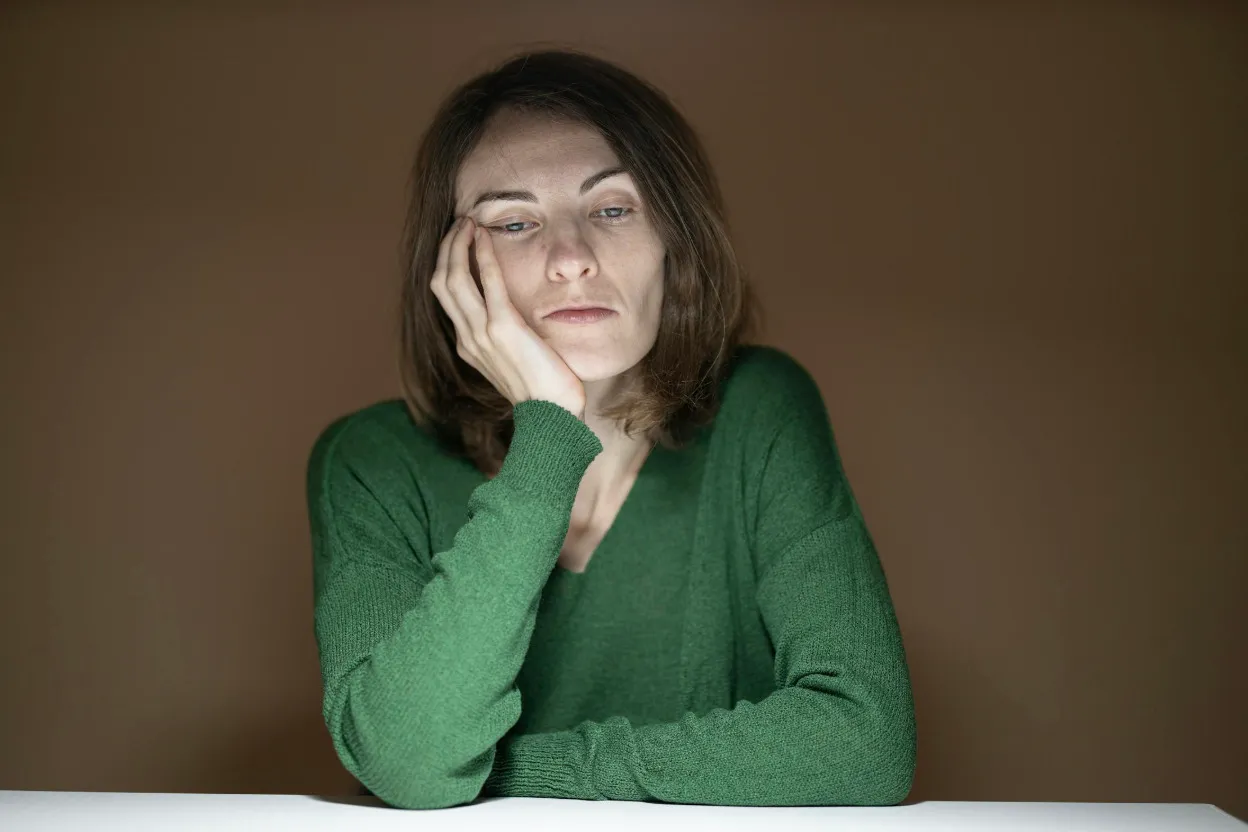 A woman in a green sweater, looking tired and deeply disappointed, resting her chin on her hand.
