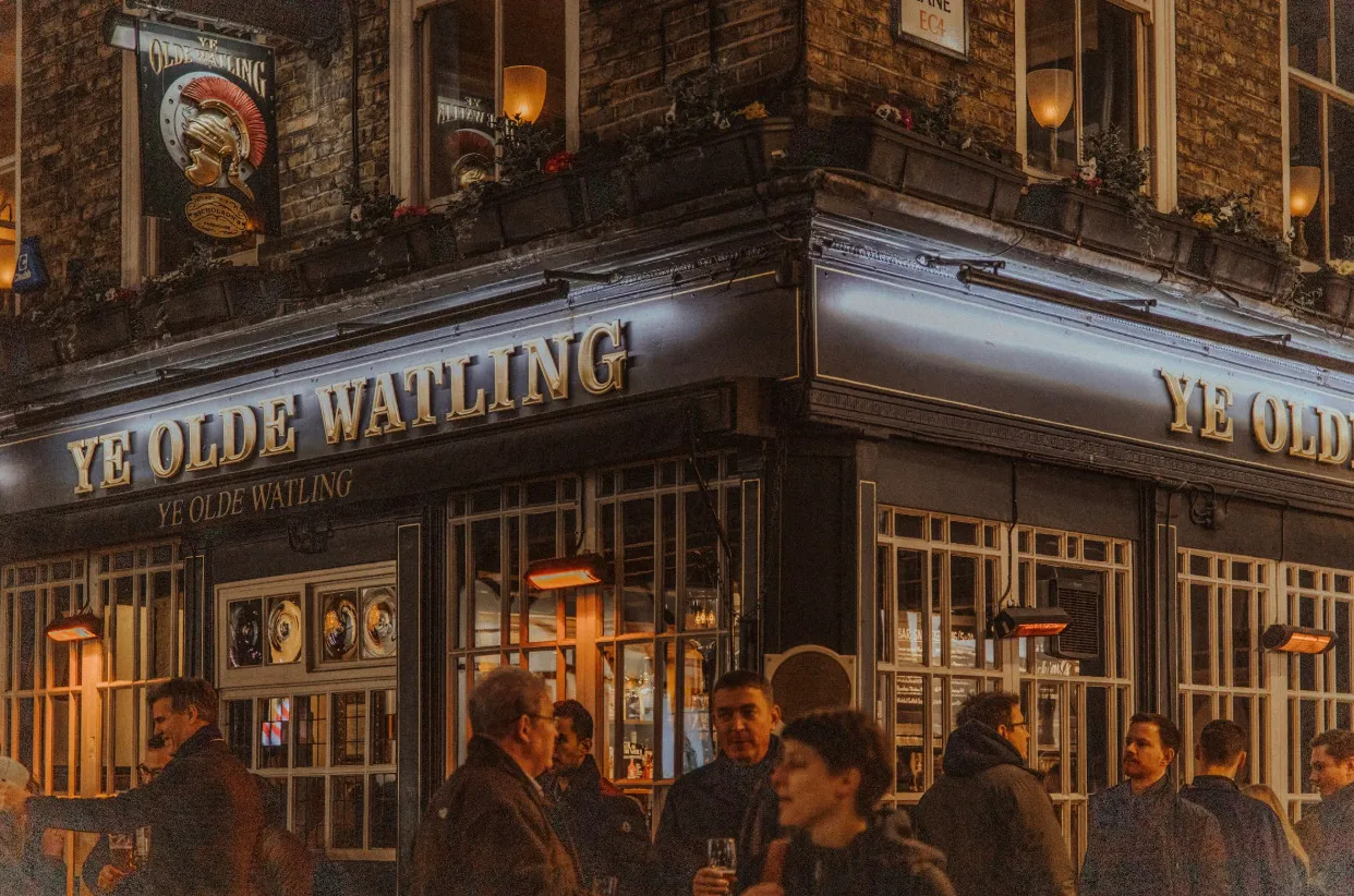 Exterior of Ye Olde Watling, a local pub with a traditional sign and people enjoying the evening, perhaps watching the telly.