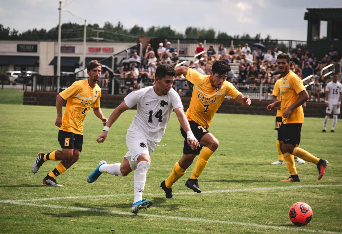 Going to a big sports event: Soccer players in white and yellow jerseys, competing for the ball on a green field.