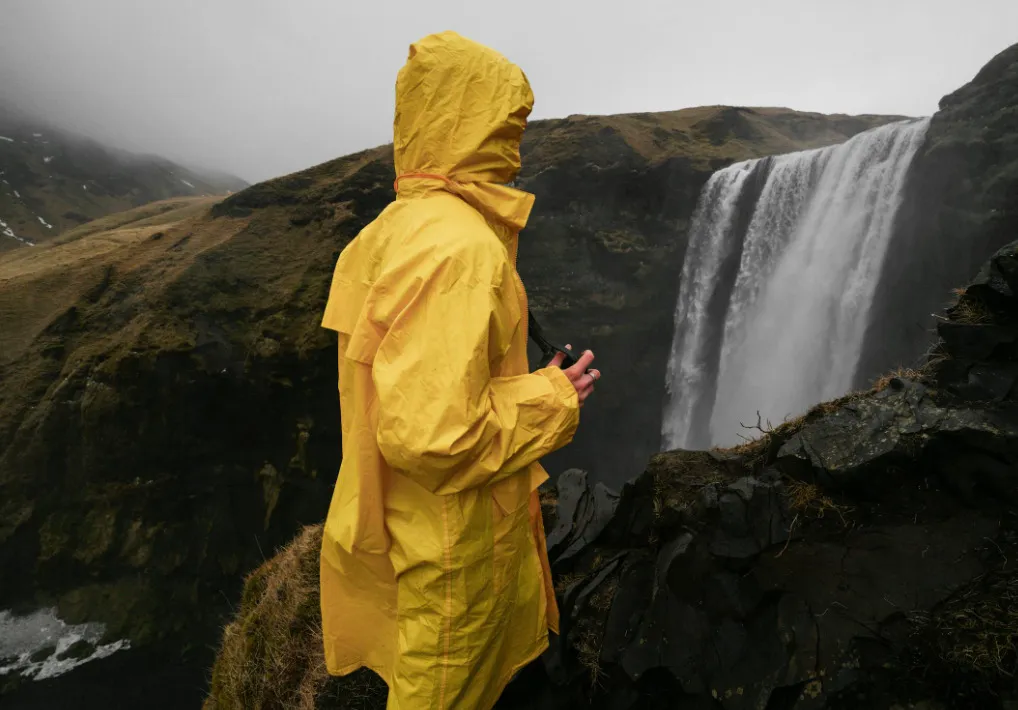 Person in a bright yellow raincoat looking at a large waterfall and misty hills. A type of raincoat.