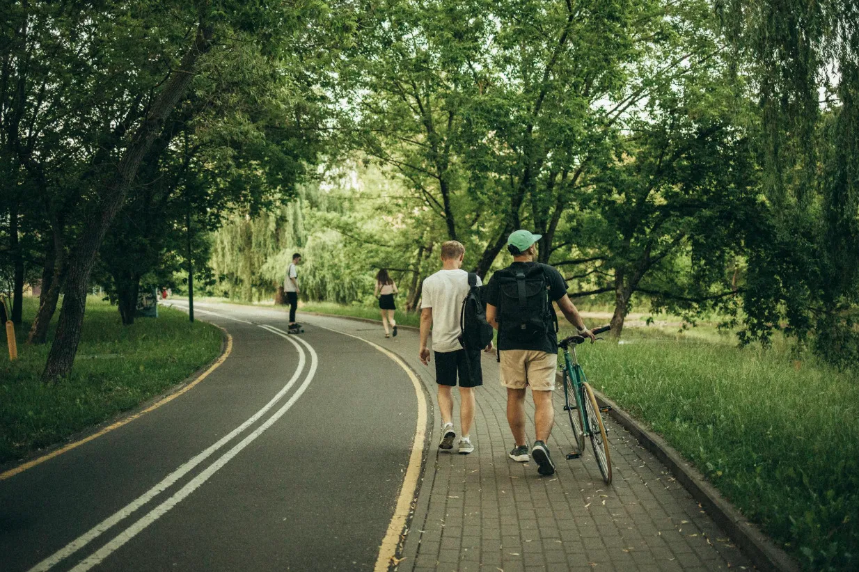 Friends enjoying a chinwag while going for a long walk in a green park, one with a bike.