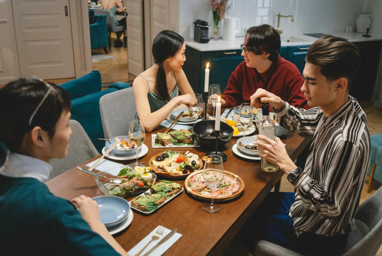 Friends enjoy a large meal together at a table laden with food and wine.