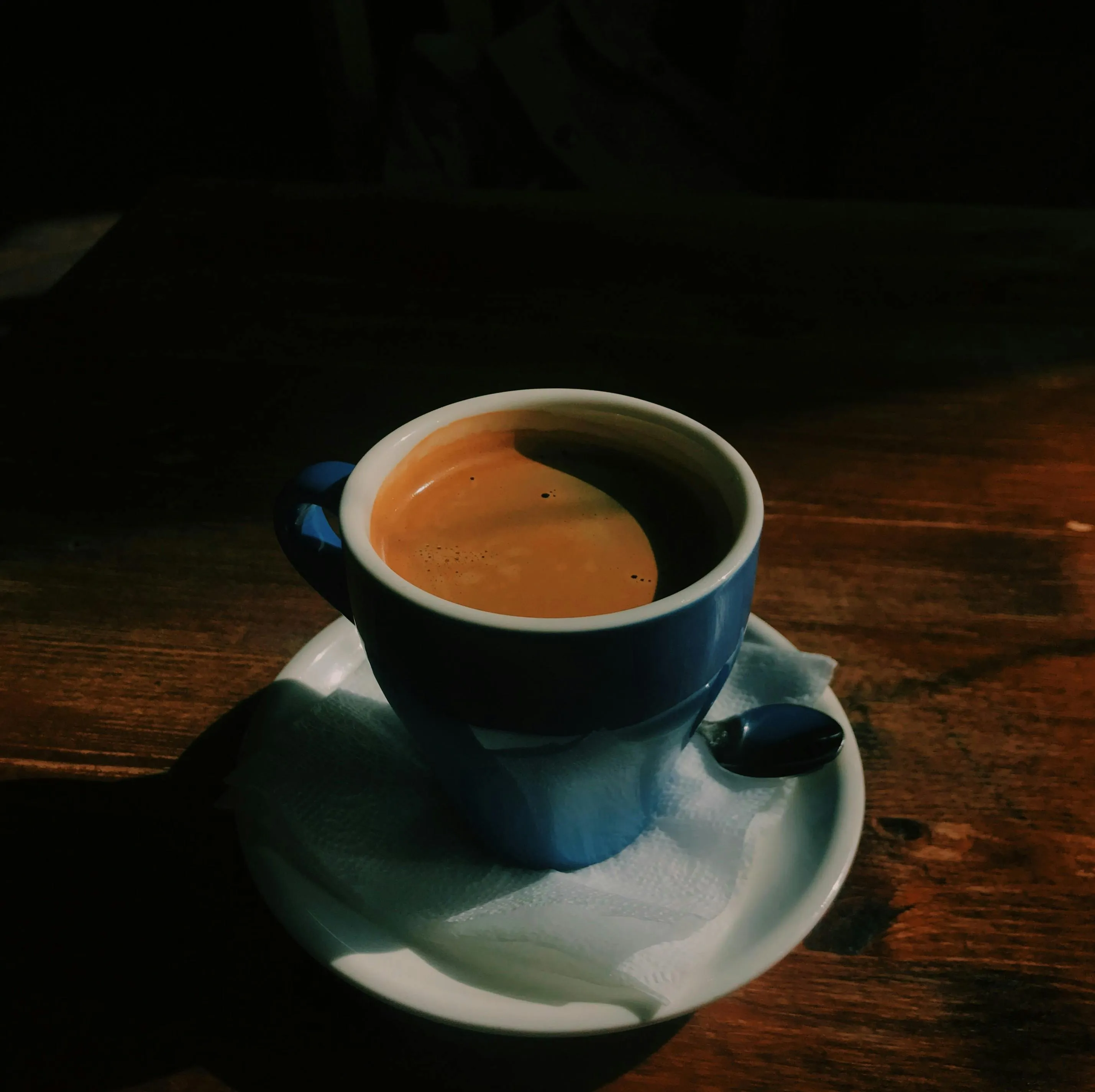 A blue cup of warm coffee on a wooden table, illuminated by a beam of sunlight. A good feeling.