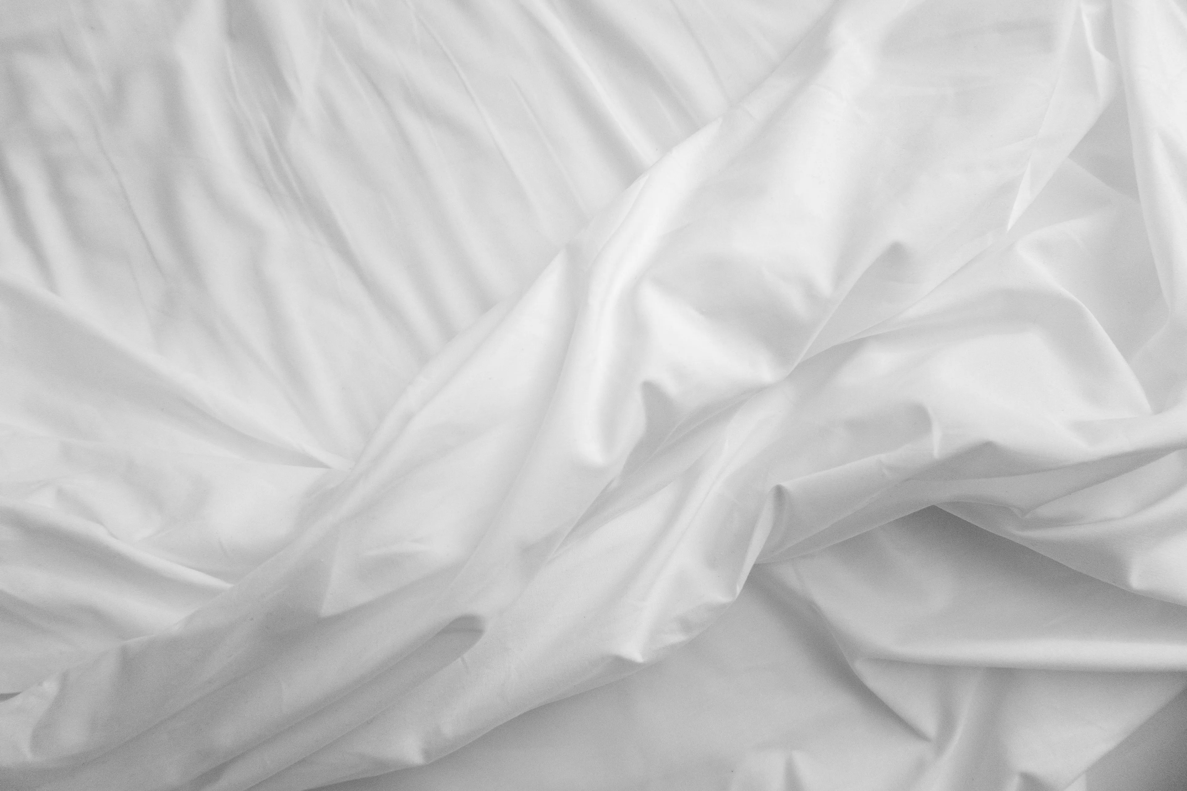 Close-up of clean sheets, featuring soft white fabric with gentle folds and shadows, evoking a good feeling.