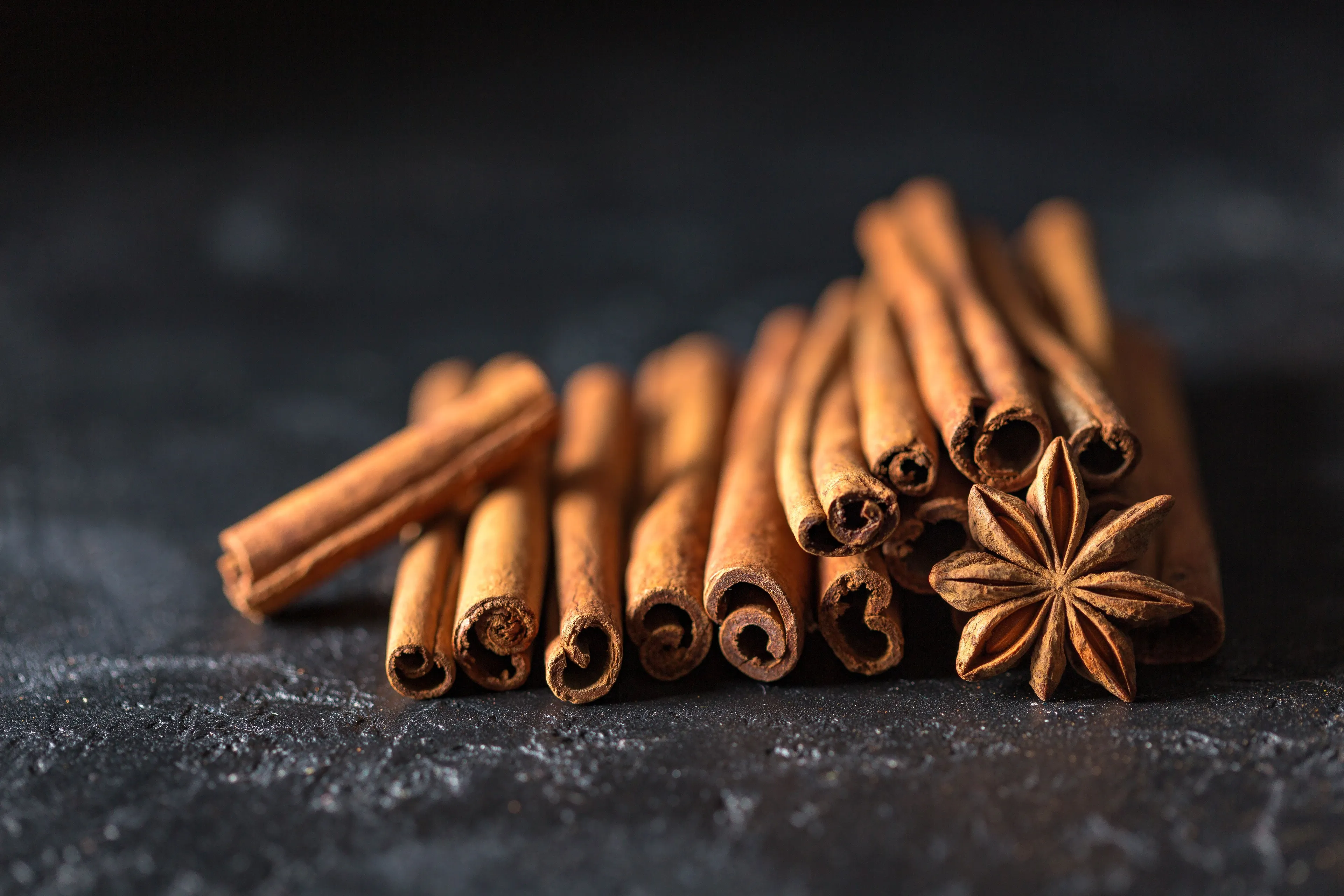 Cinnamon sticks and a star anise pod on a dark stone surface, evoking a good feeling and warmth.
