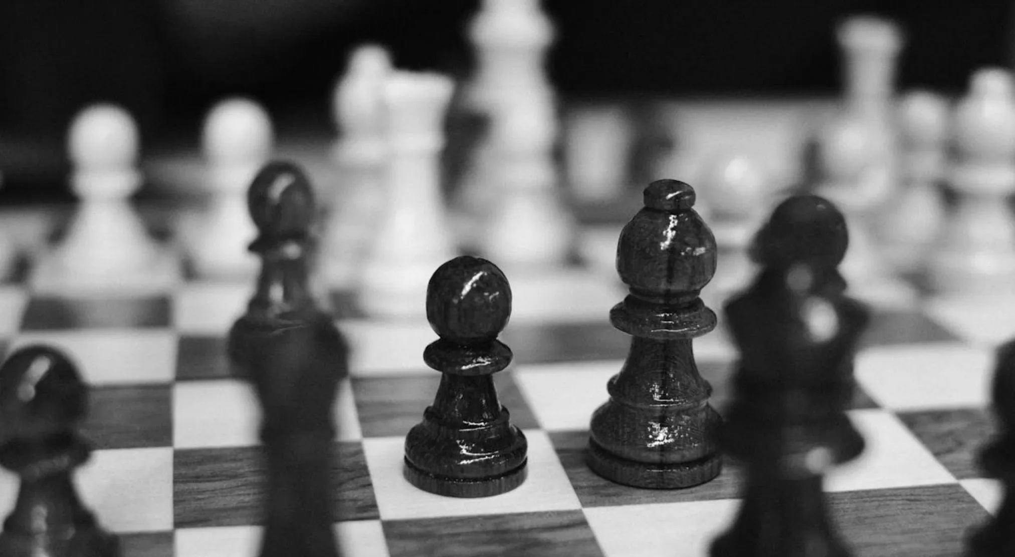 A close-up, black and white photo of chess pieces on a chessboard, focusing on the dark pawn and bishop. How many individual playing squares does a standard chessboard have?