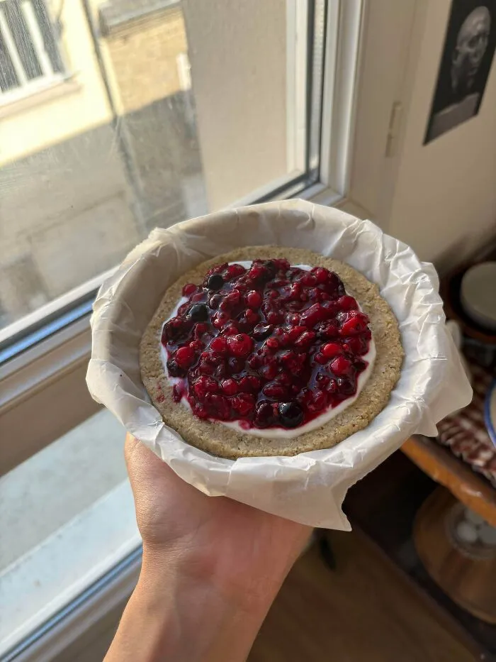 Amazing treats by bakers: A person holds a small, round pastry with berries and cream, a delicious treat.