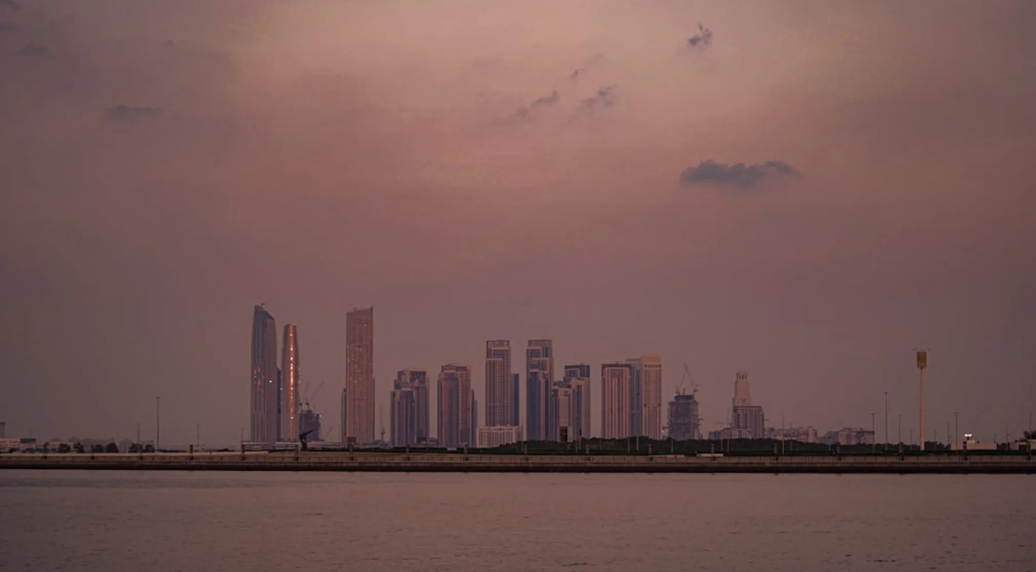 Skyscrapers stand tall against a twilight sky, reflecting light over water. This image represents the UAE and its emirates.