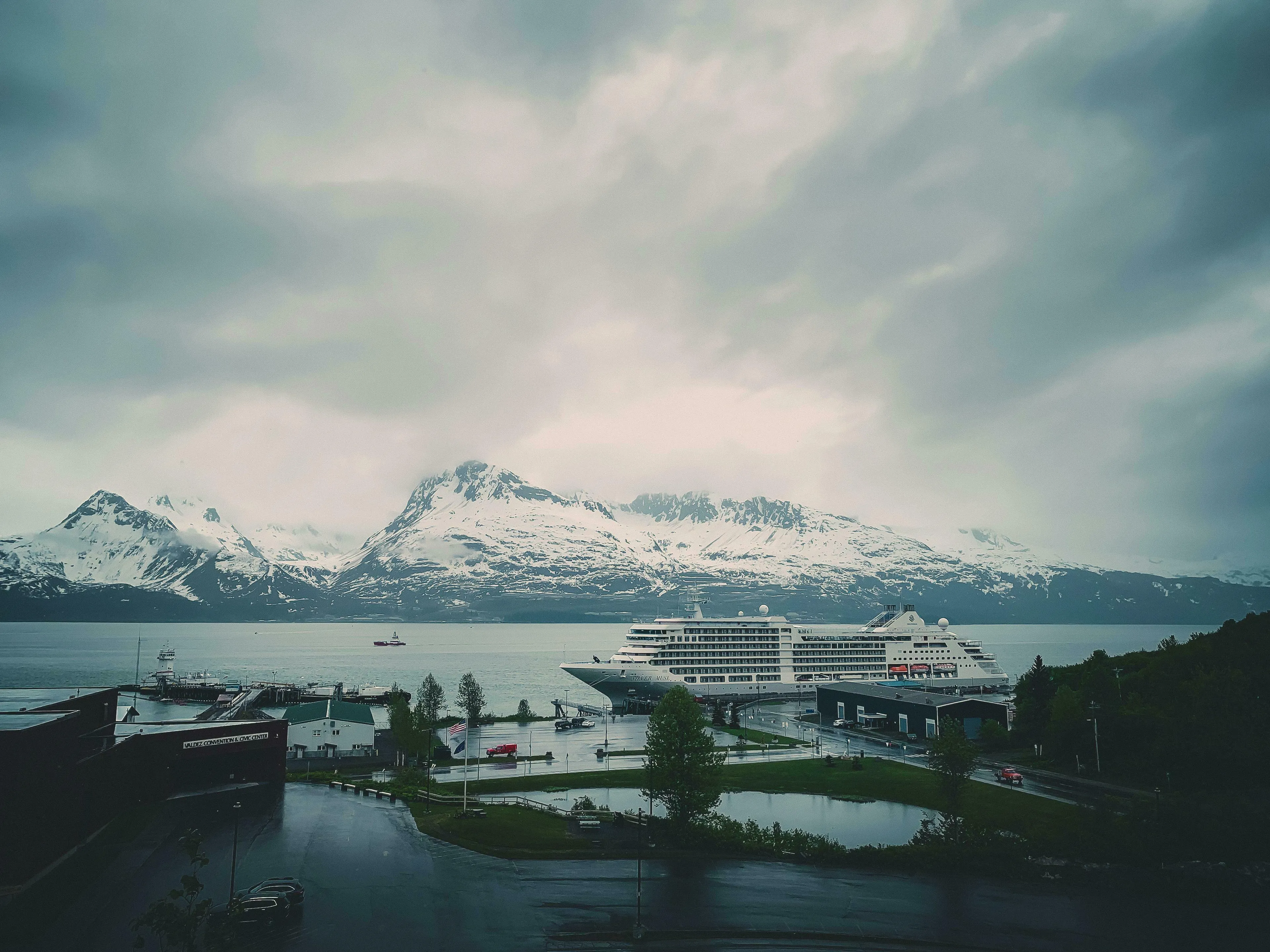 A cruise ship docked in an Alaskan port with snow-capped mountains and a cloudy sky. US state capitals quiz answer.
