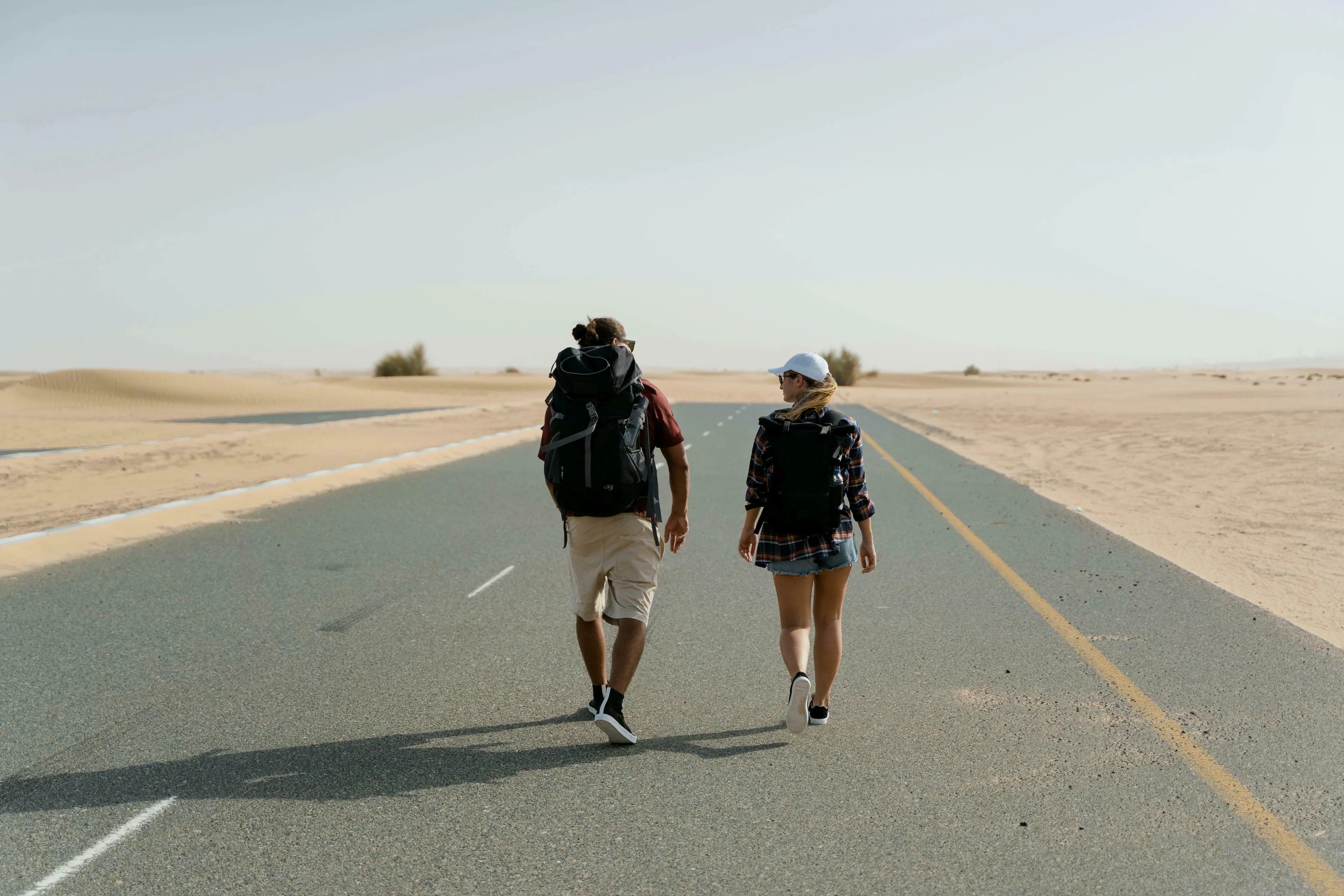 A man and woman with backpacks walk down a long desert road, on a long journey, pondering their medieval profession.