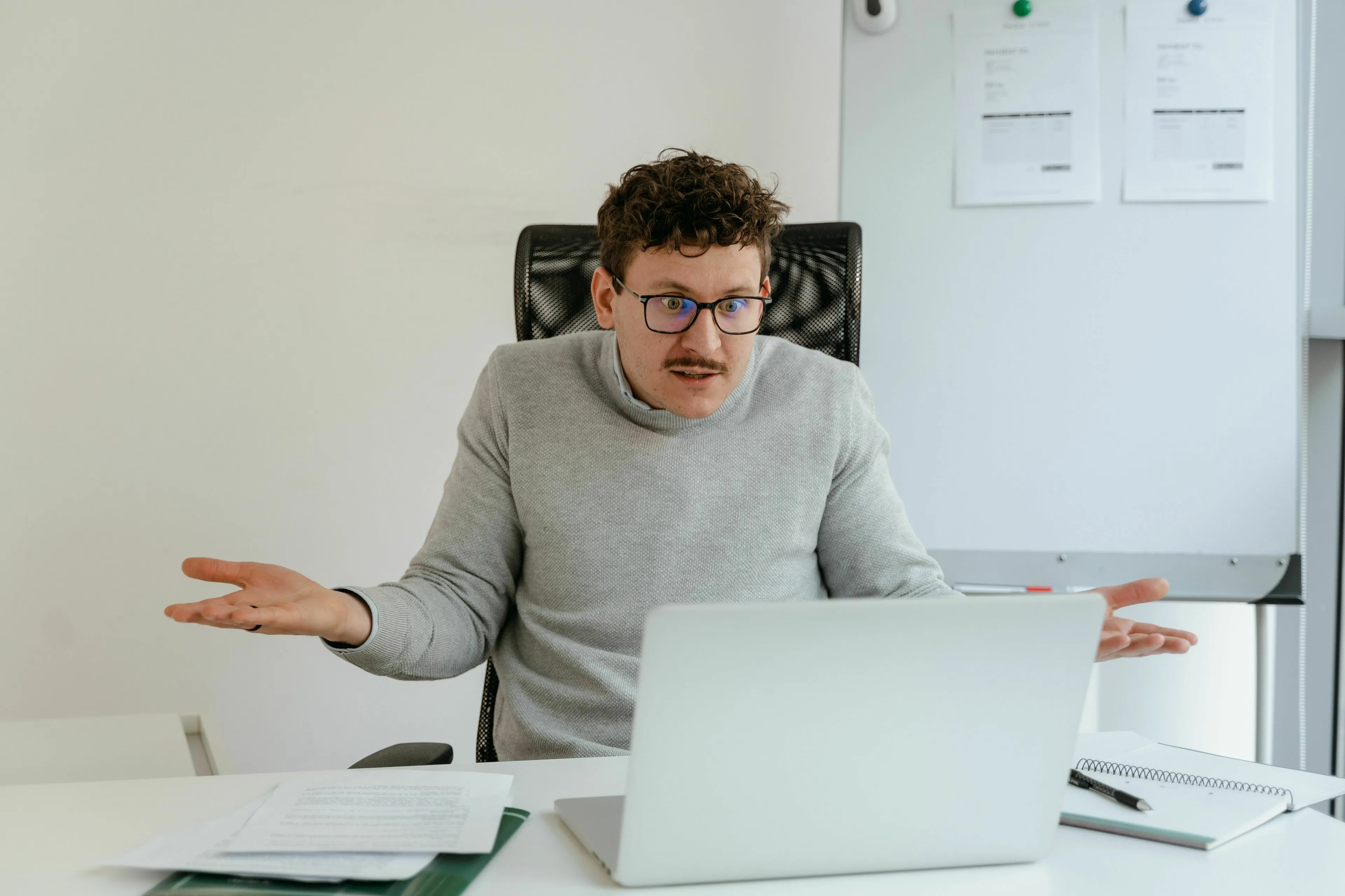 A man with glasses and a mustache, sitting at a desk with a laptop, shrugging with an unsure expression about a medieval profession.