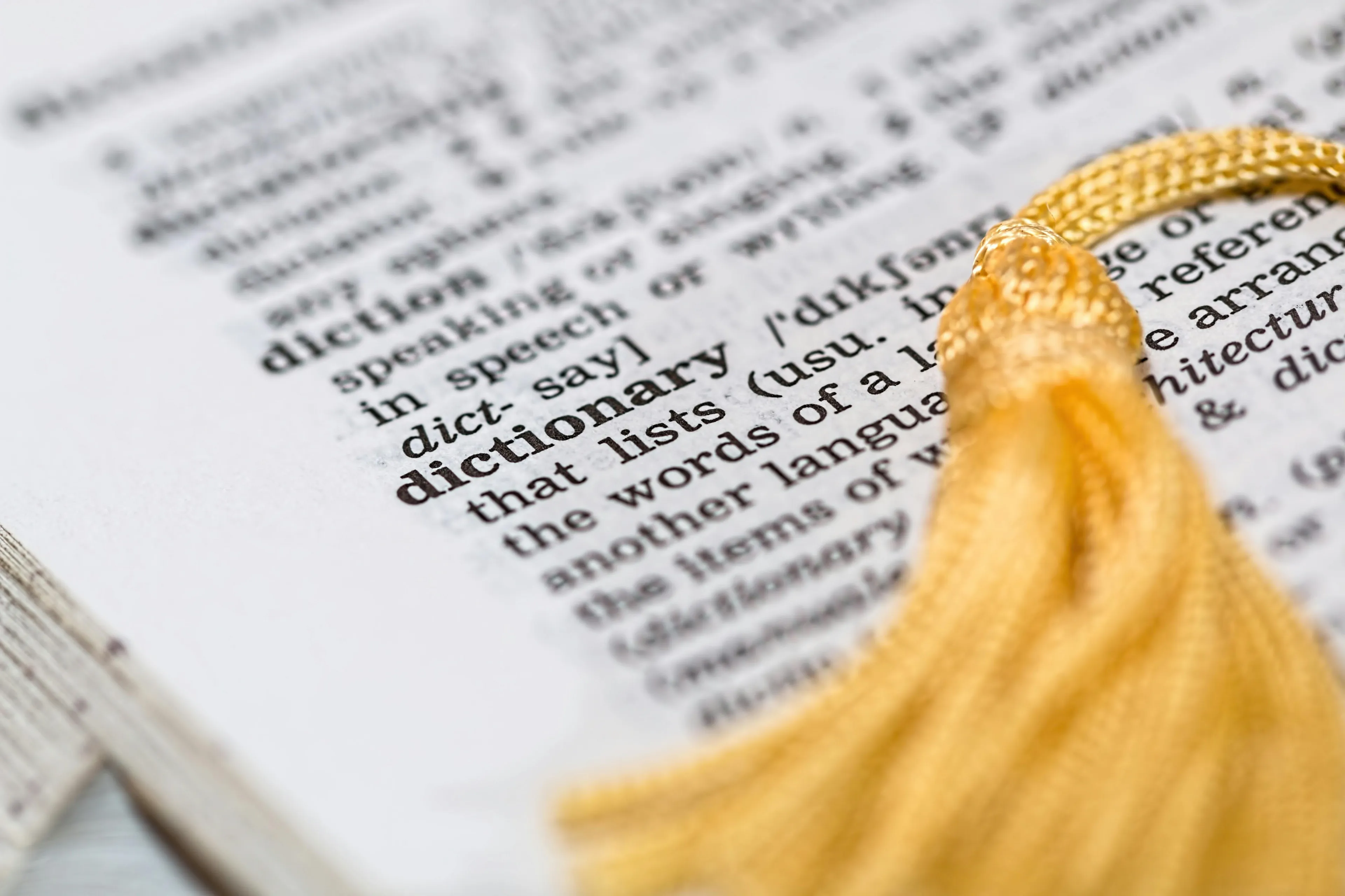Close-up of a dictionary page with the word dictionary defined. A gold tassel bookmark is visible, symbolizing the desire for mastering skills like speaking multiple languages.