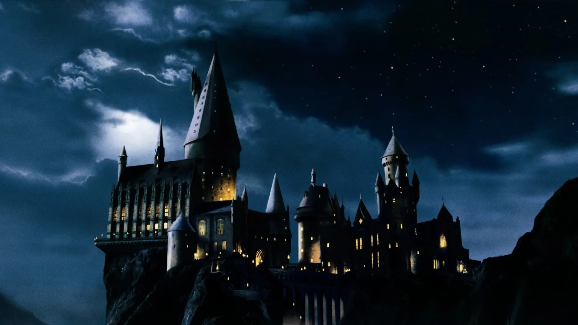 Hogwarts castle at night, illuminated against a dark, cloudy sky with faint stars, evoking a sense of magic.