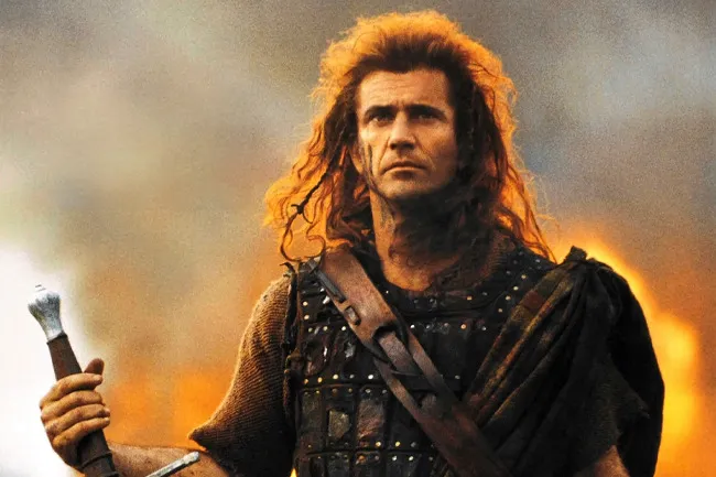 Mel Gibson as William Wallace in Braveheart, holding a sword with a fiery background.