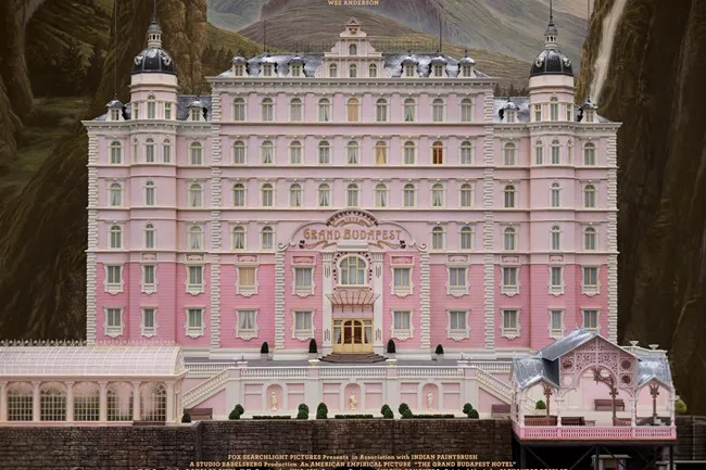 A magnificent pink and white hotel from The Grand Budapest Hotel movie, set against a mountainous backdrop.