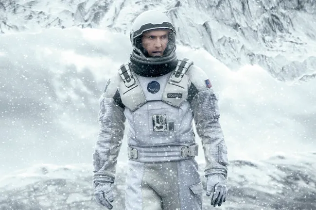 Matthew McConaughey as Cooper in a white astronaut suit from Interstellar, amidst a snowy, mountainous landscape.