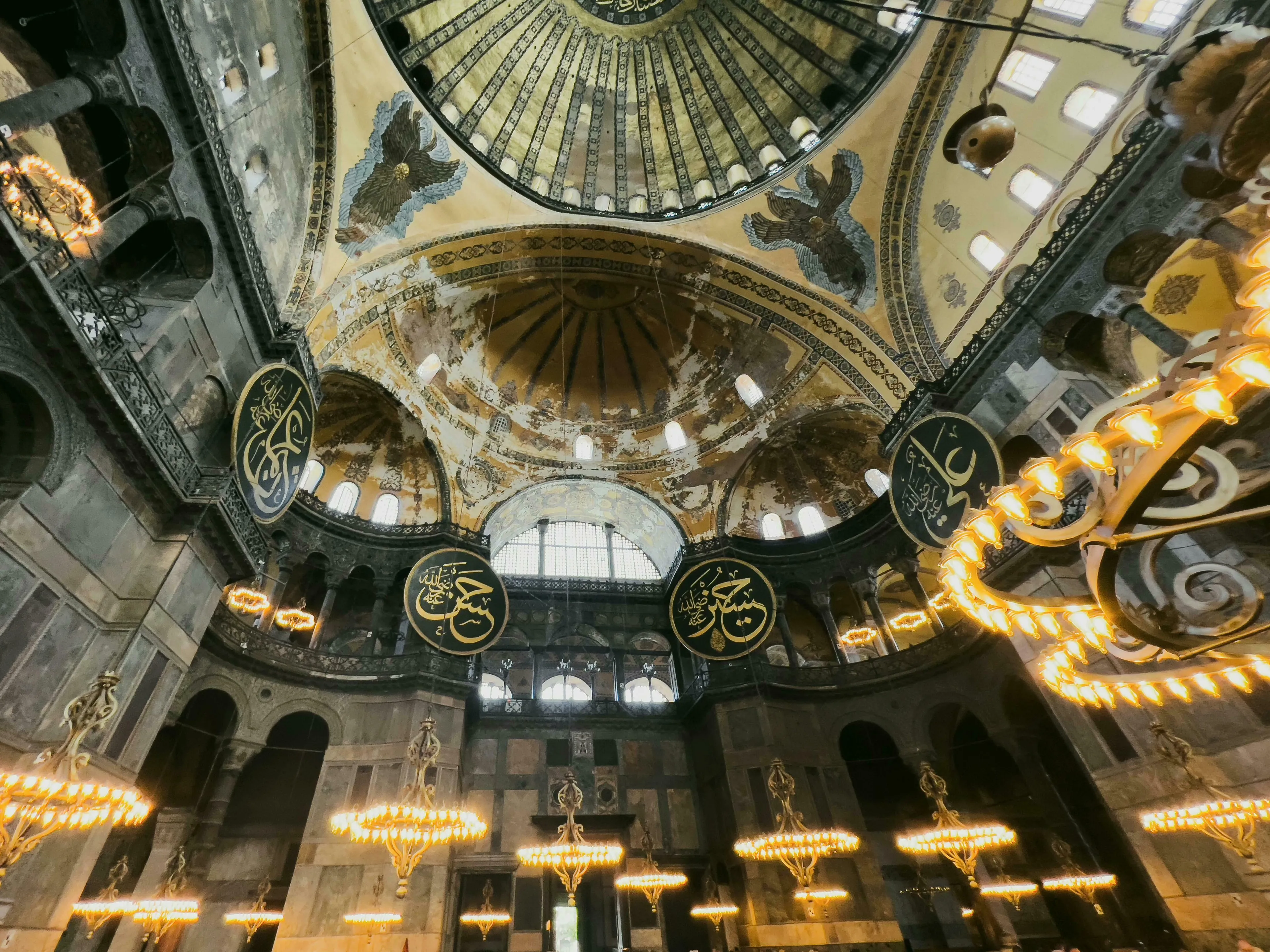 Interior view of the Hagia Sophia, showcasing its grand dome, intricate calligraphy, and numerous chandeliers. General Knowledge Quiz.