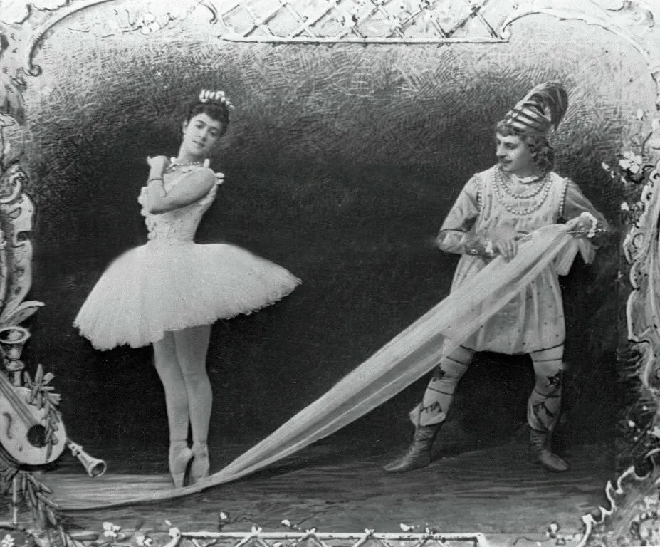 Black and white photo of a ballerina en pointe with a male performer in costume holding a long veil. Nutcracker.