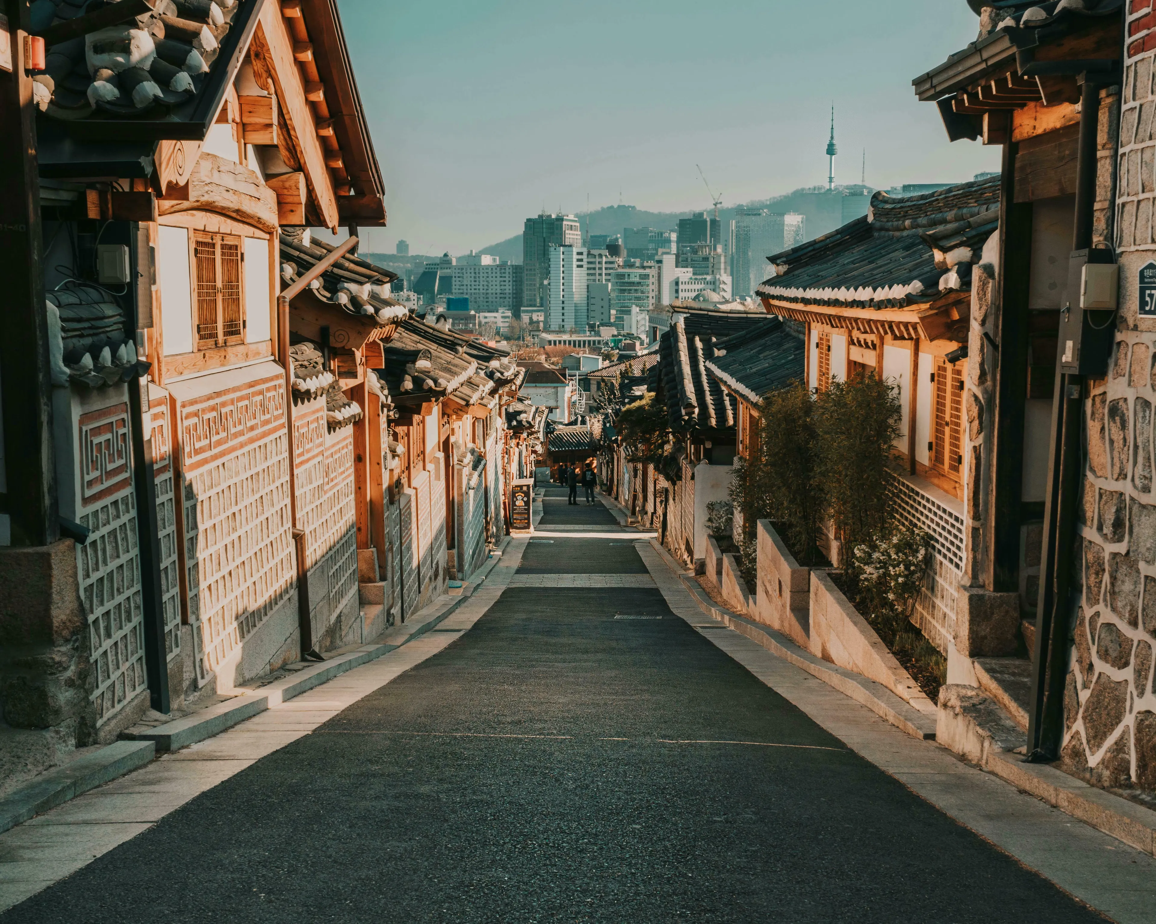 A traditional Korean village street with modern city buildings and the Seoul Tower in the background. What is the currency of Korea?