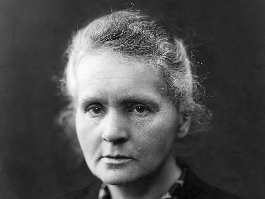 A black and white close-up portrait of Marie Curie, the first woman to win a Nobel Prize, looking directly at the viewer.