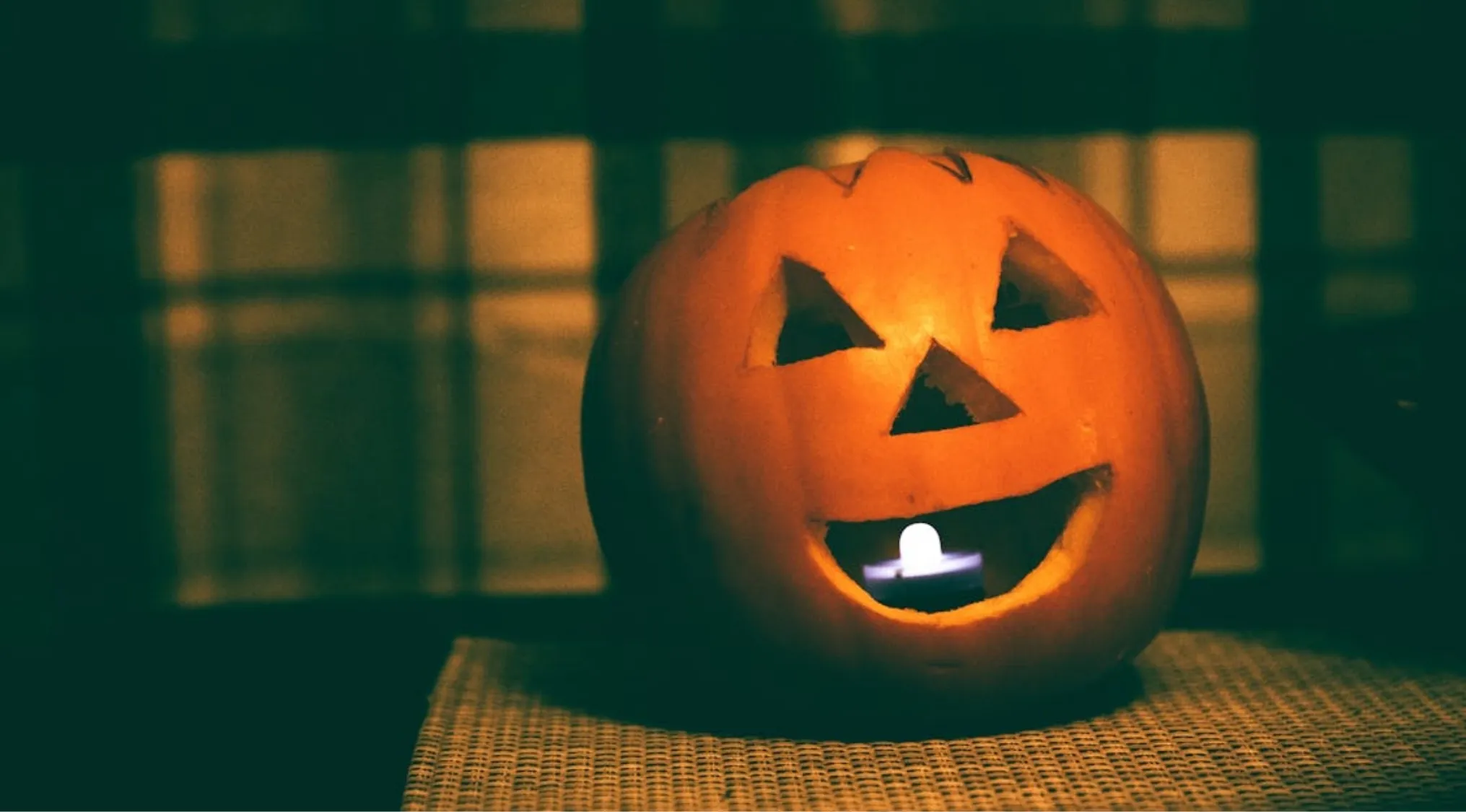 A smiling pumpkin face carved for Halloween, lit by a candle from within, creating a warm glow. Living in America.