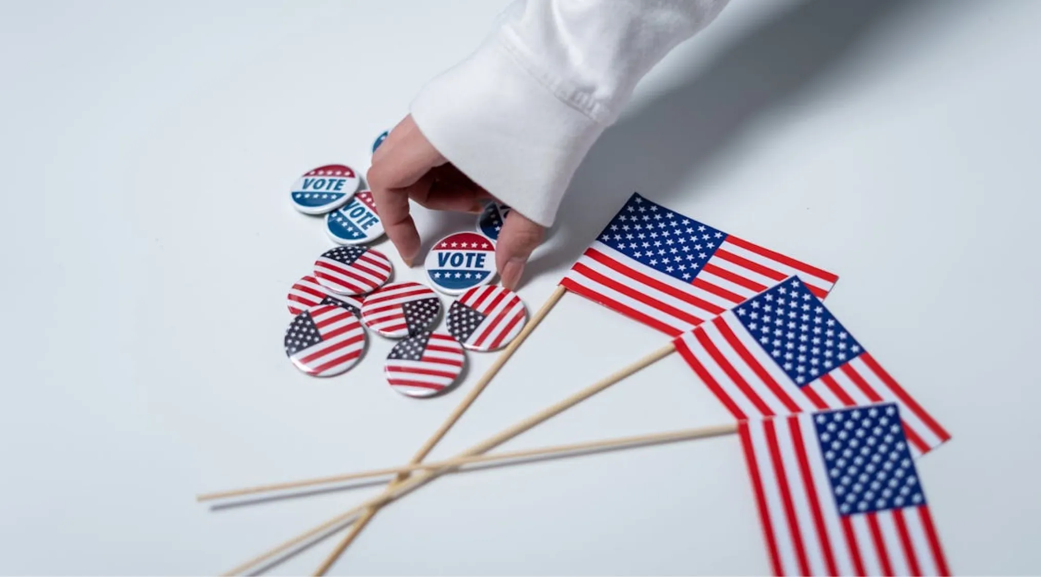 Hand placing a vote button among other American flag pins and small US flags. Living in America election.