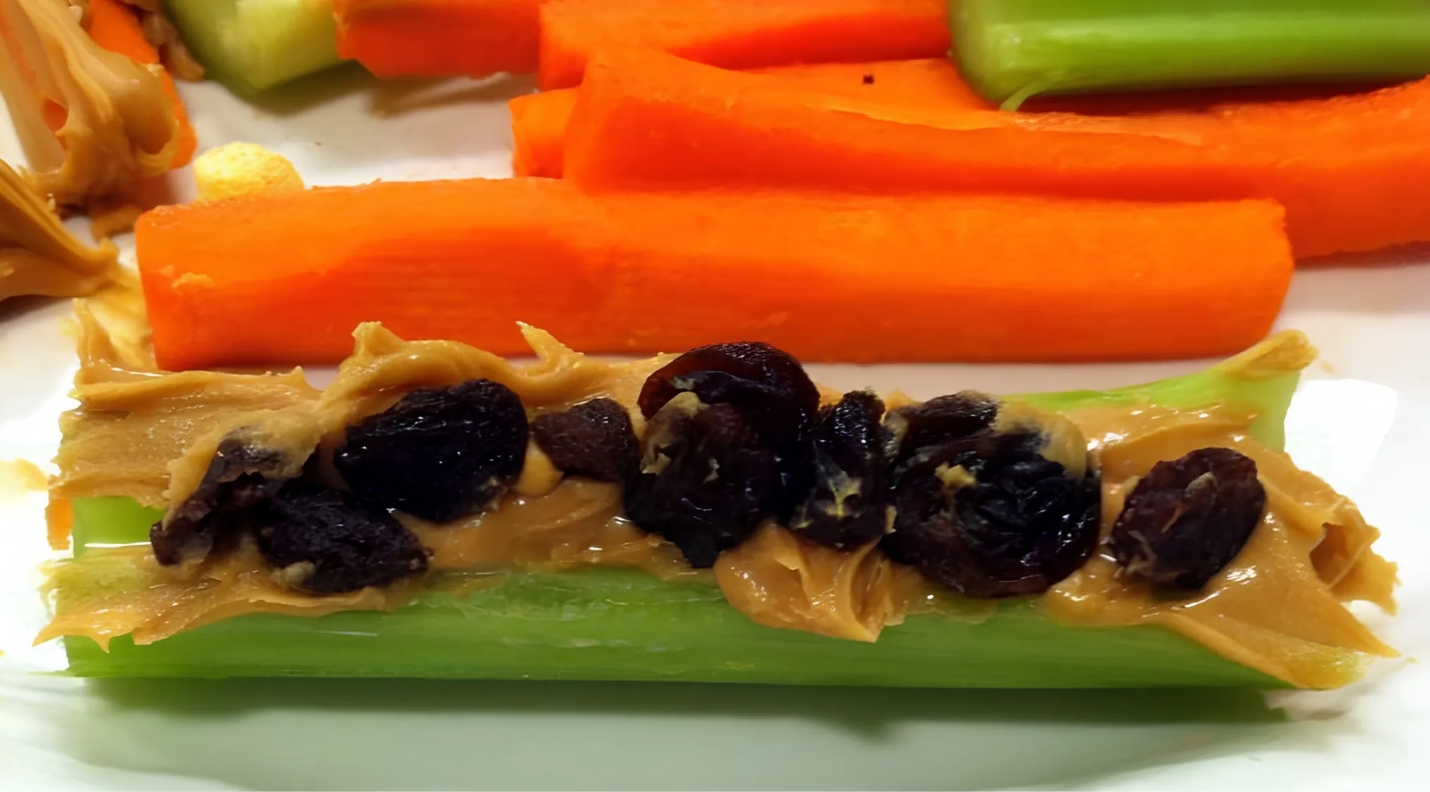 Ants on a log snack: celery sticks with peanut butter and raisins, alongside carrot and cucumber sticks. Living In America.