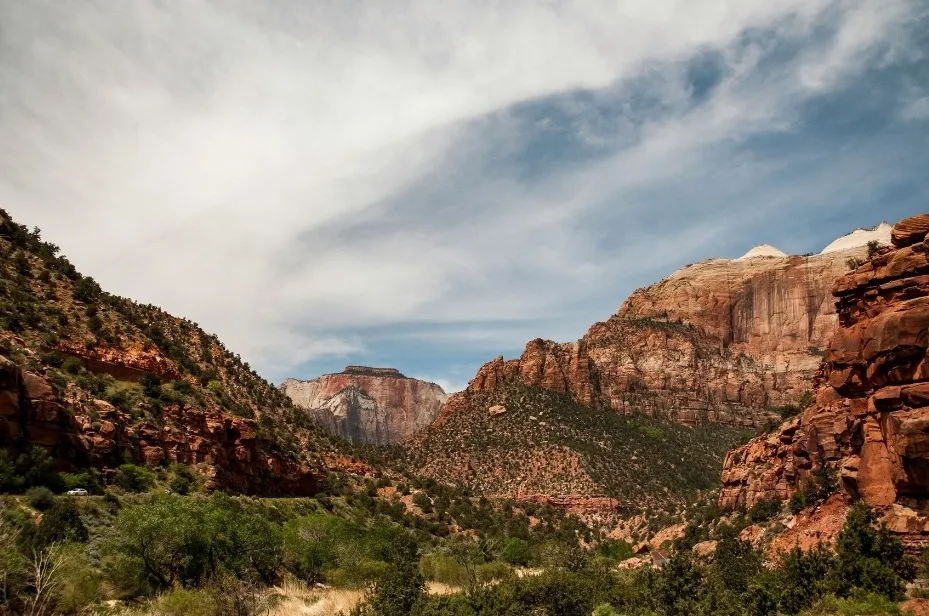 Zion national park, a stunning vista of majestic red cliffs and lush green valleys under a blue, cloudy sky.